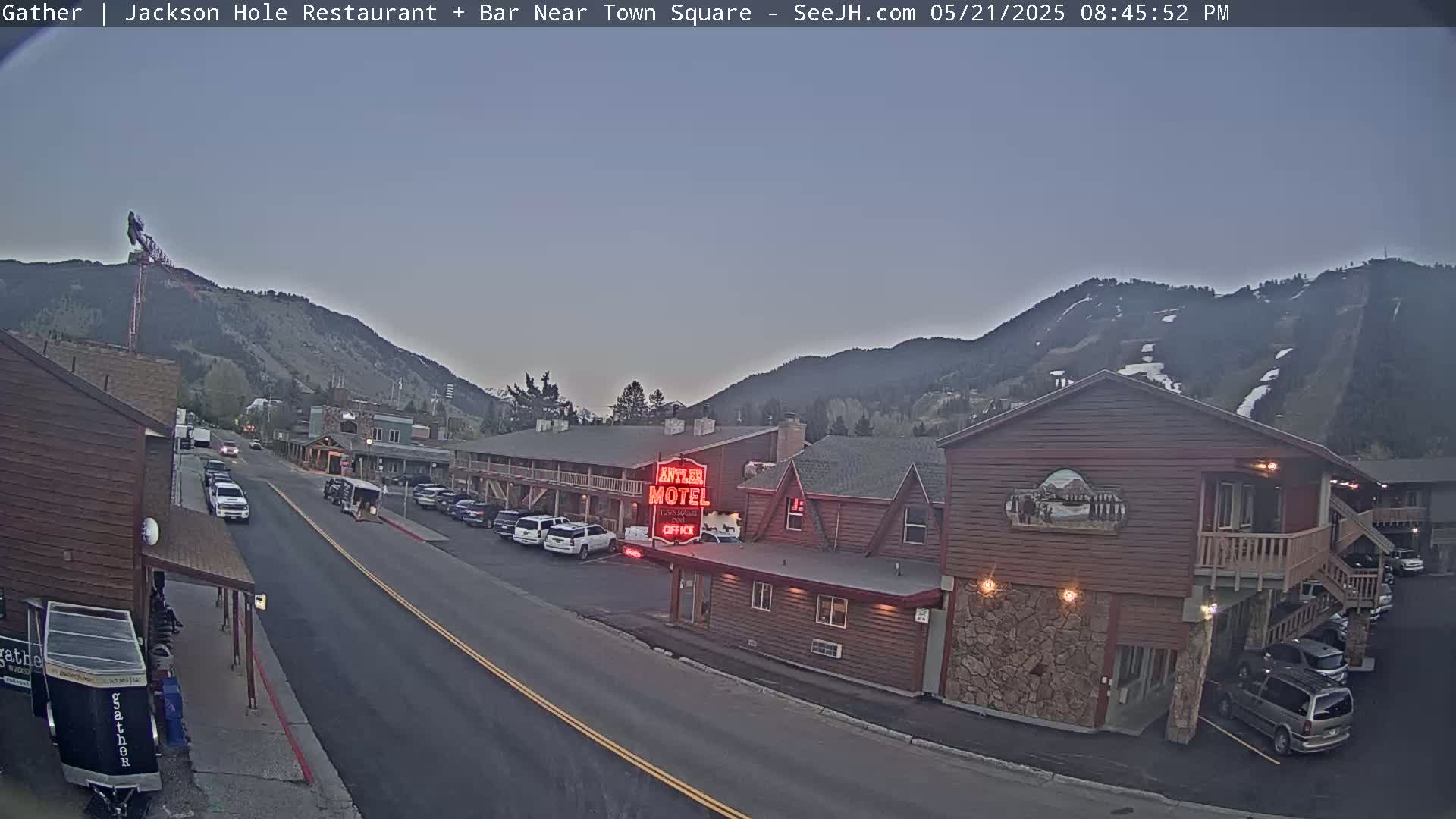 A street scene at dusk shows a motel and parked cars, with mountains in the background under a clear, twilight sky.