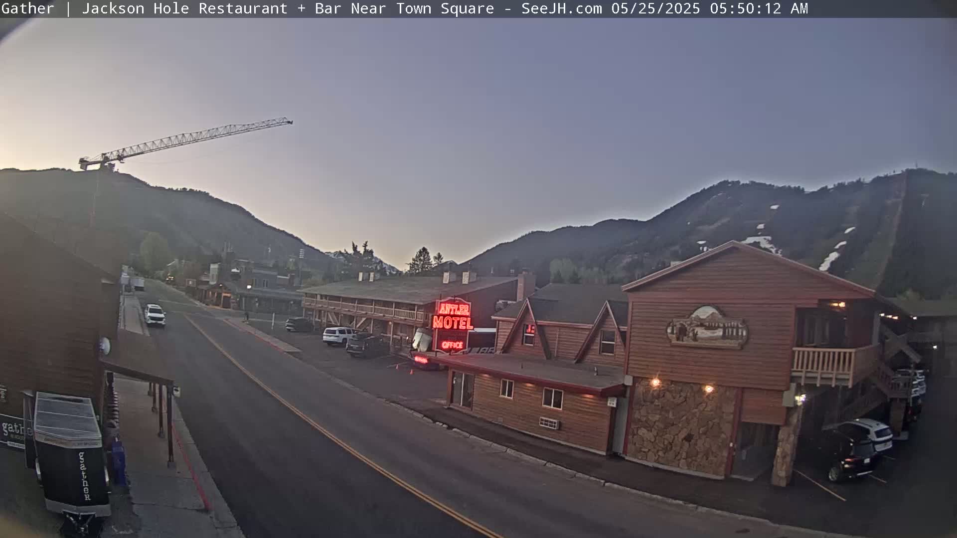 A street scene at dawn shows a motel, cars, and a construction crane against a backdrop of mountains.
