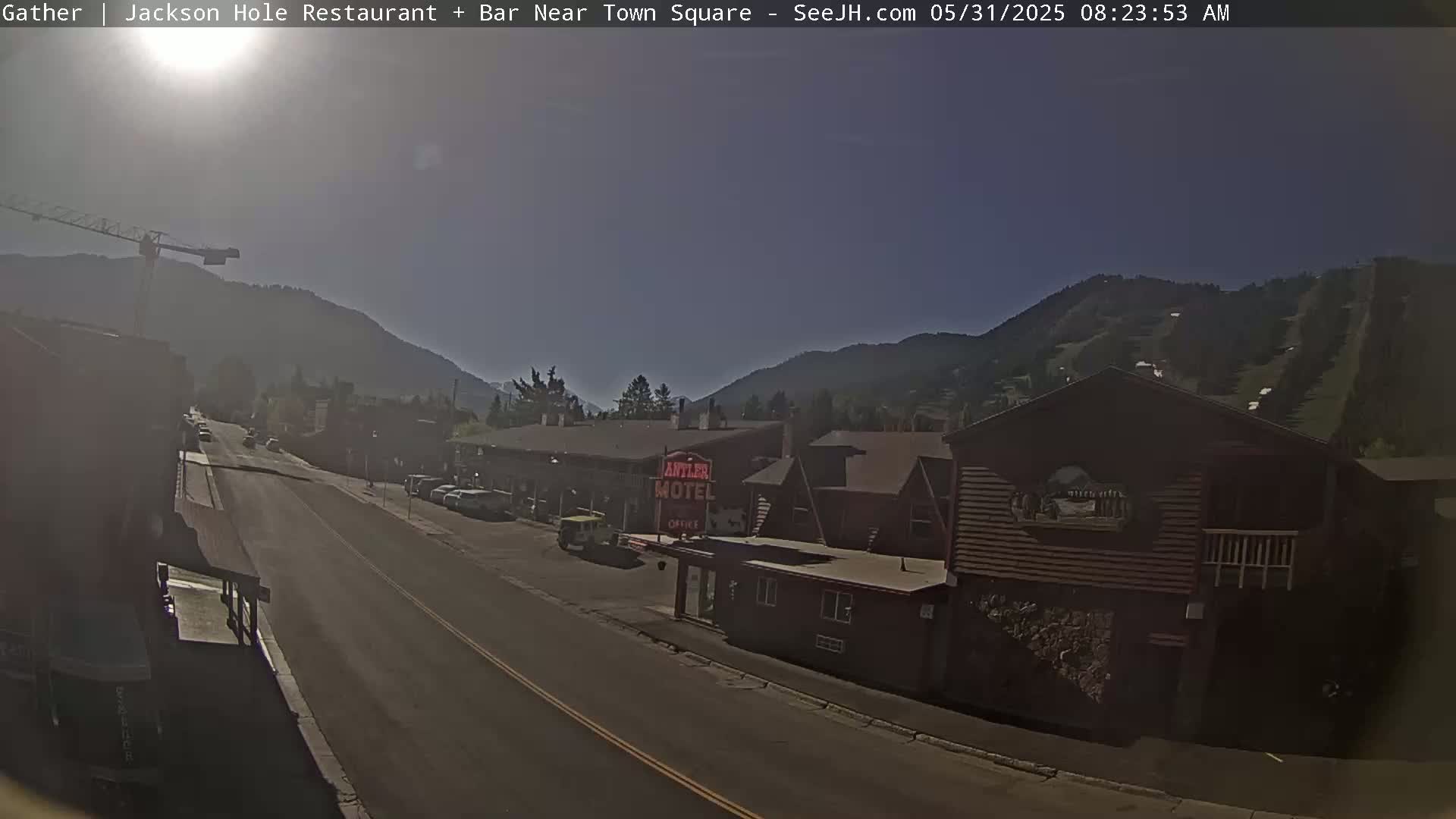 A sunny morning view of a town street with a motel and mountains in the background.