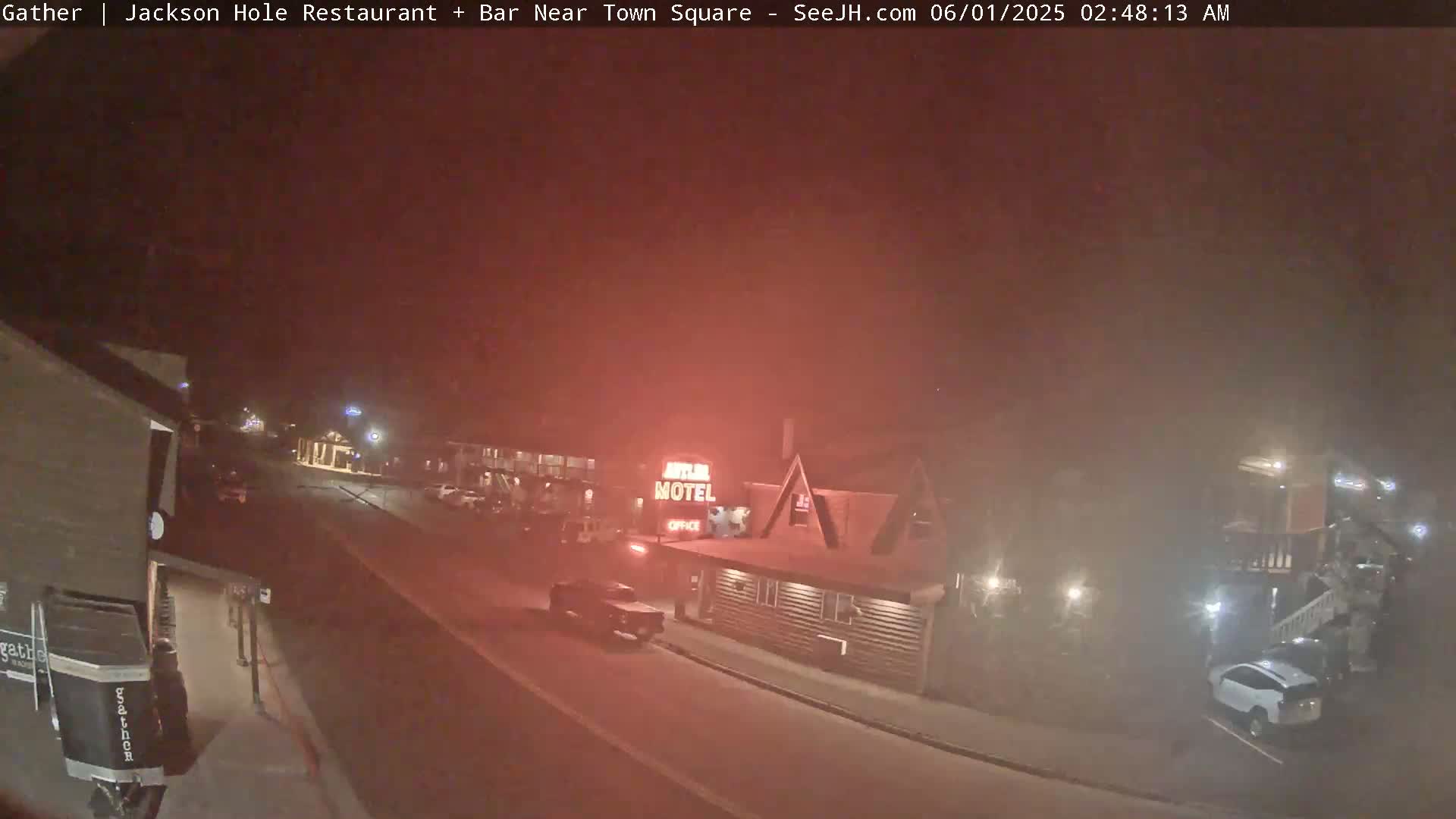 A nighttime, hazy street scene shows a motel and several vehicles parked along the road.