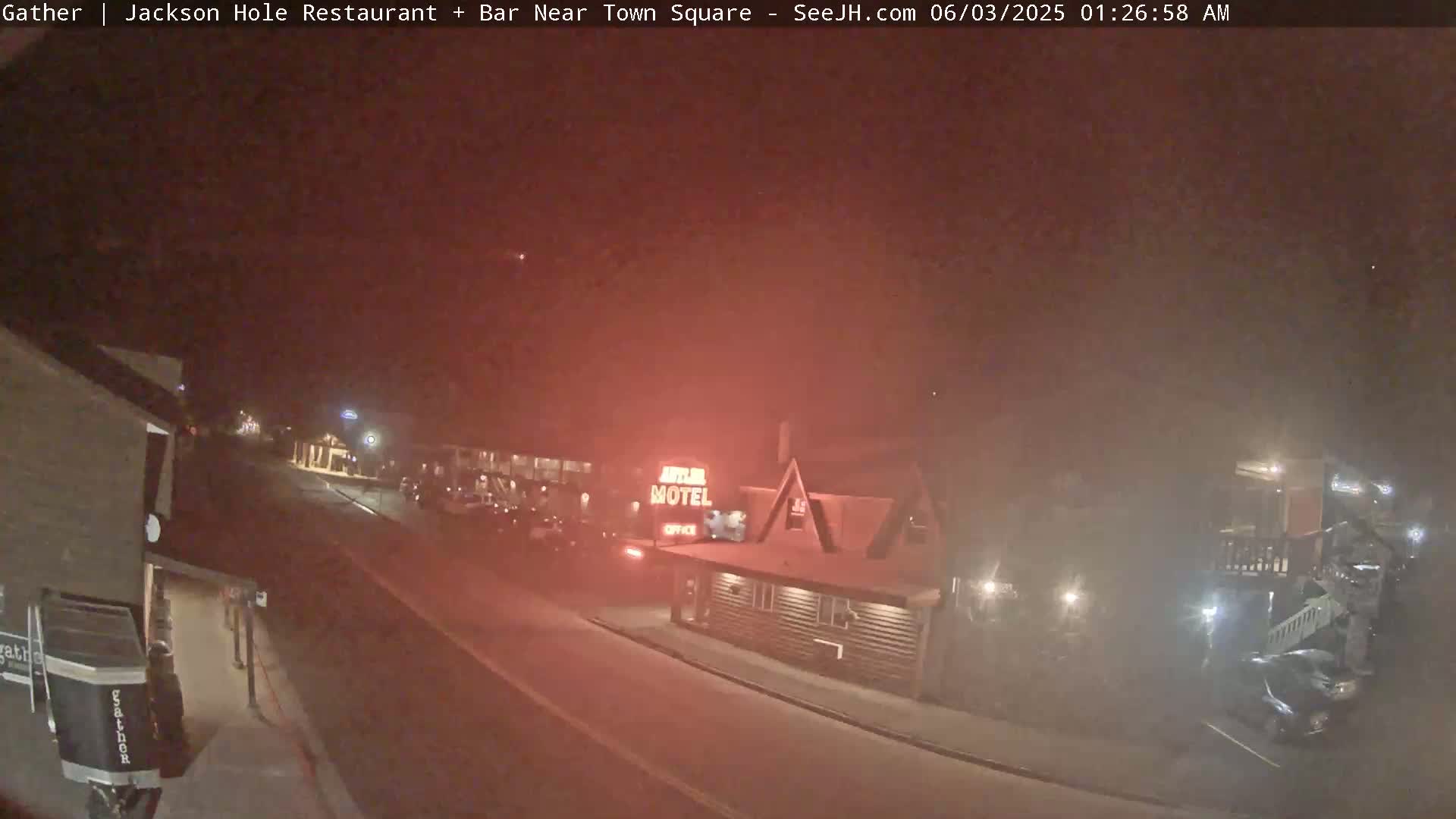 A nighttime, hazy view of a street scene showing a motel and parked cars.