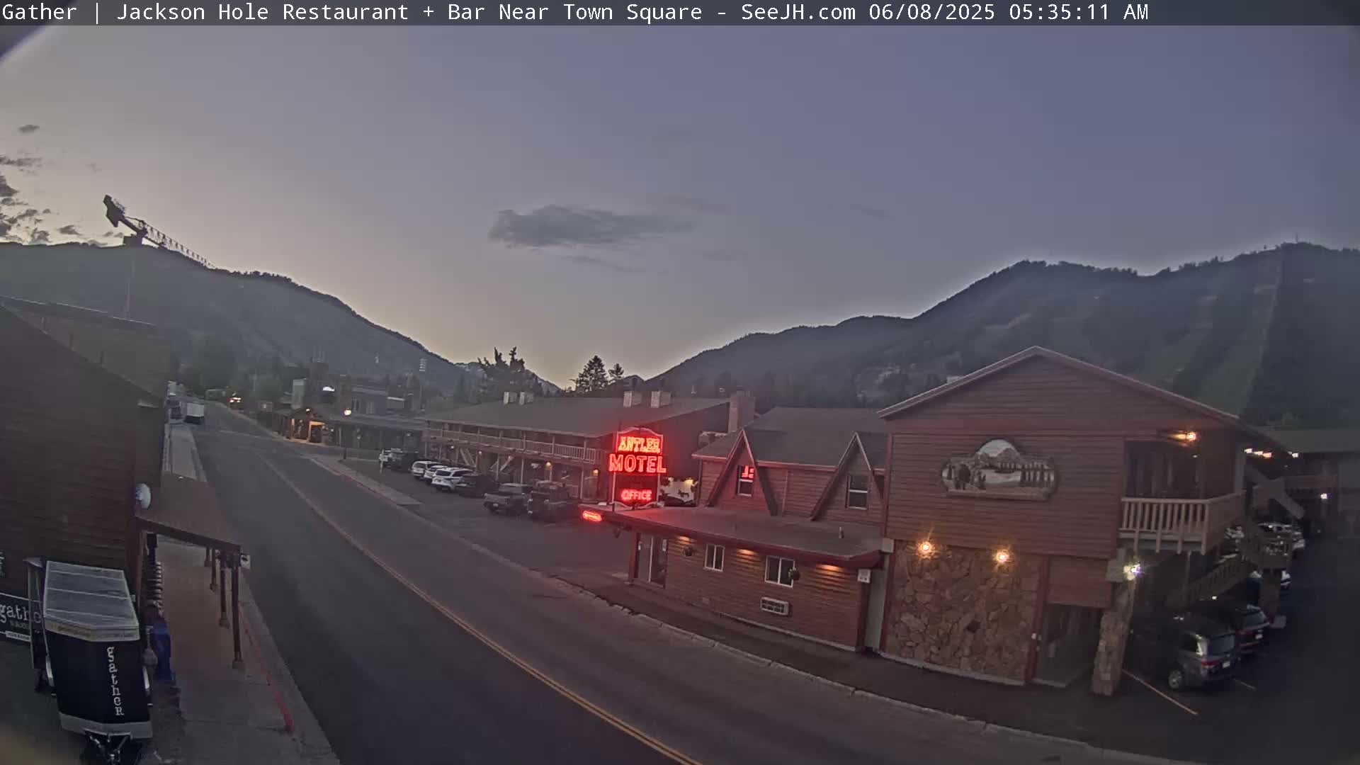 A street scene at twilight shows a motel and other buildings nestled between mountains under a clear, dusky sky.