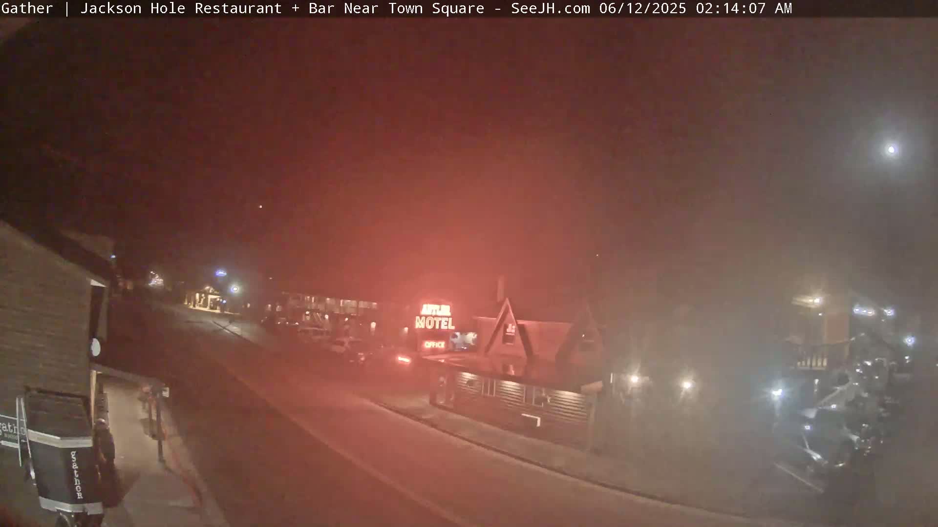 A foggy night scene shows a street with cars and a motel, with dim lighting illuminating the area.