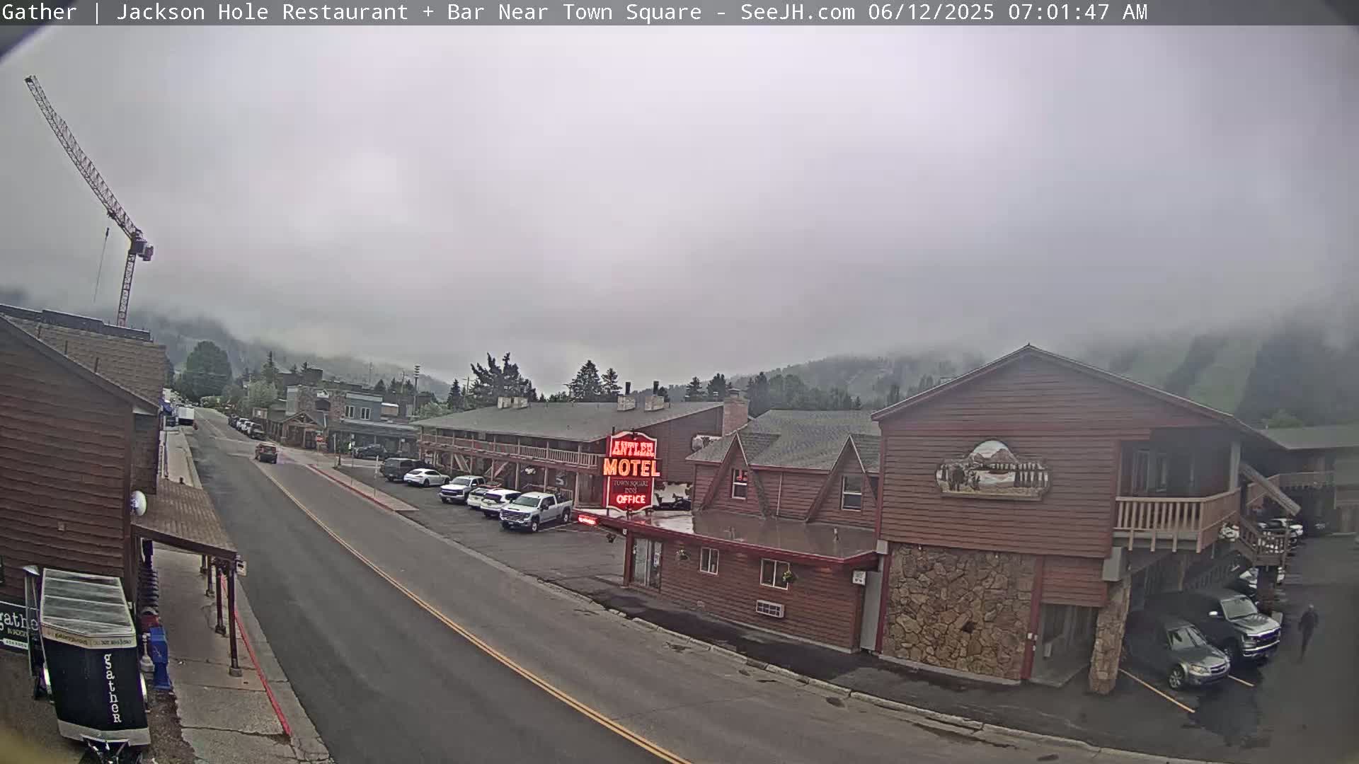 A foggy morning scene shows a street with parked cars and a motel, with a construction crane visible in the distance.