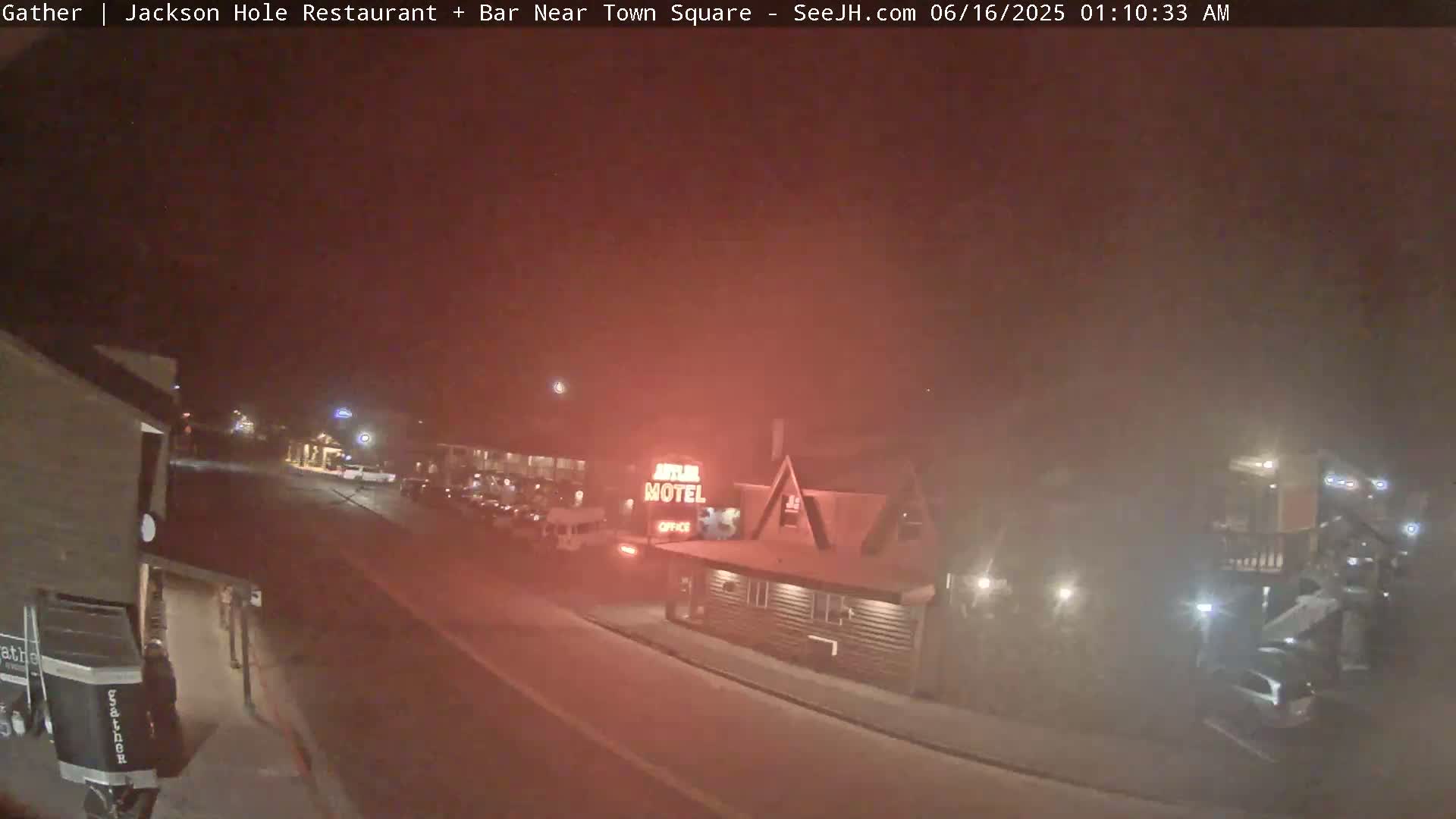 A nighttime street scene with hazy or foggy conditions shows a motel and several parked cars.