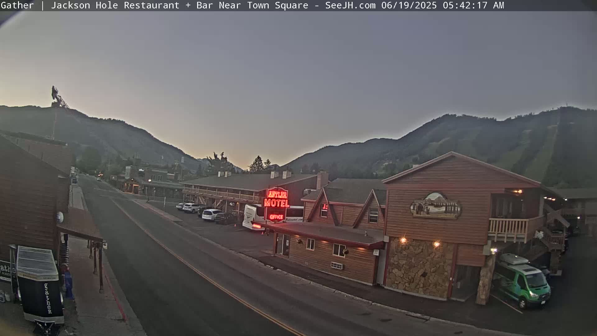 A street scene at dawn shows a motel and other buildings nestled in a valley, with mountains in the background under a dusky sky.