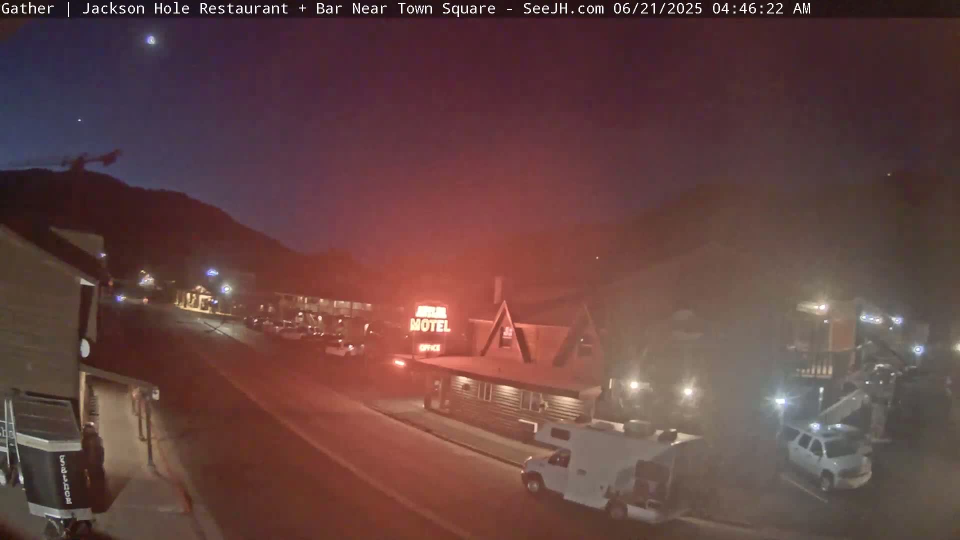 A nighttime, hazy view of a street with parked cars and a motel, under a dark, mostly clear sky.