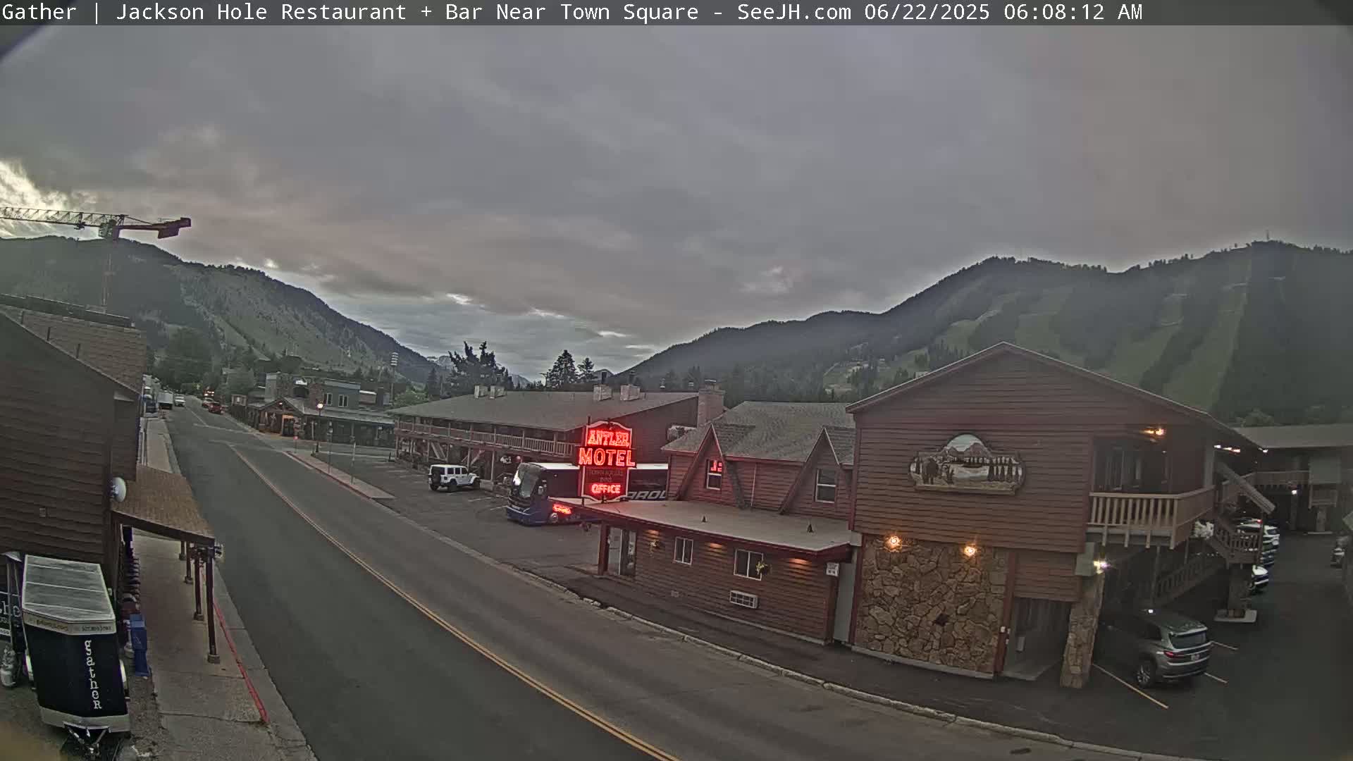 A mostly cloudy morning scene shows a street in a mountainous town, with a motel and vehicles visible, along with a construction crane in the distance.