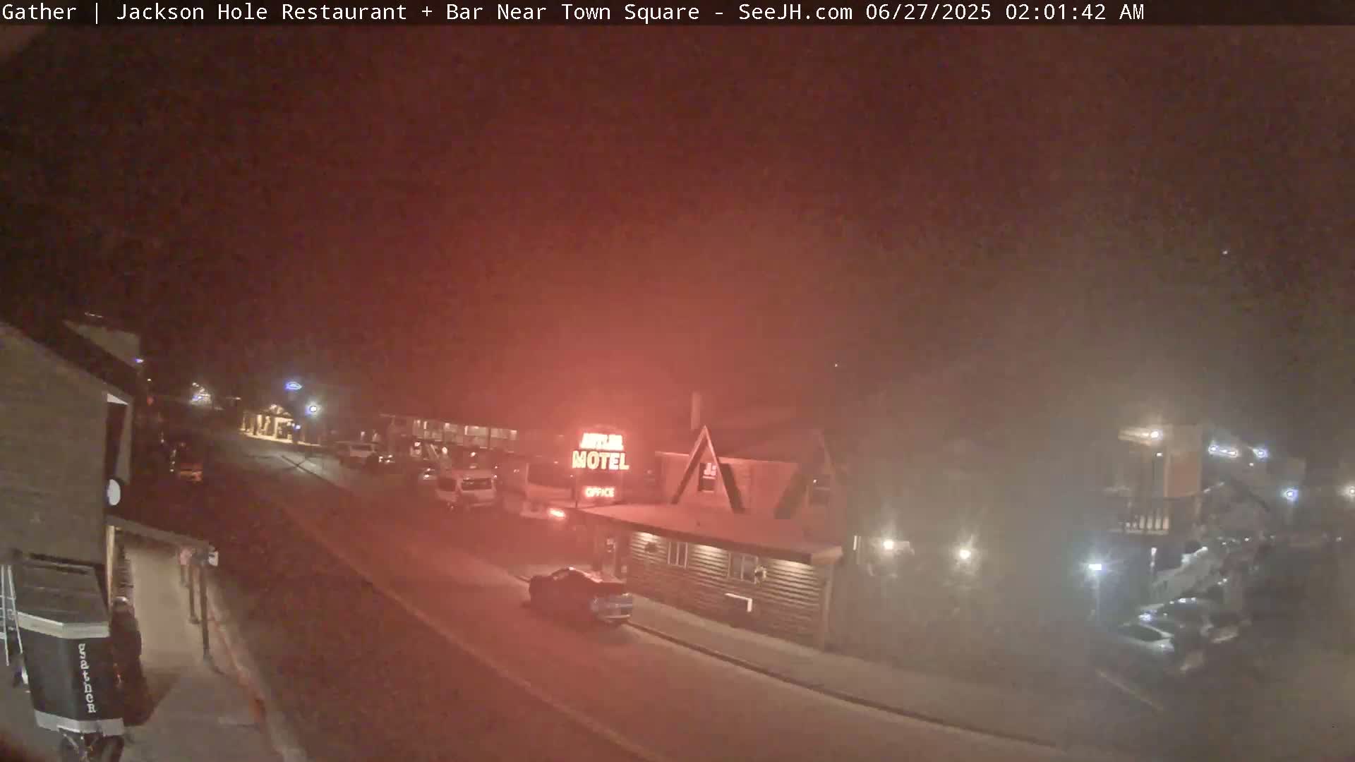 A nighttime street scene in hazy conditions shows a motel and several parked vehicles.