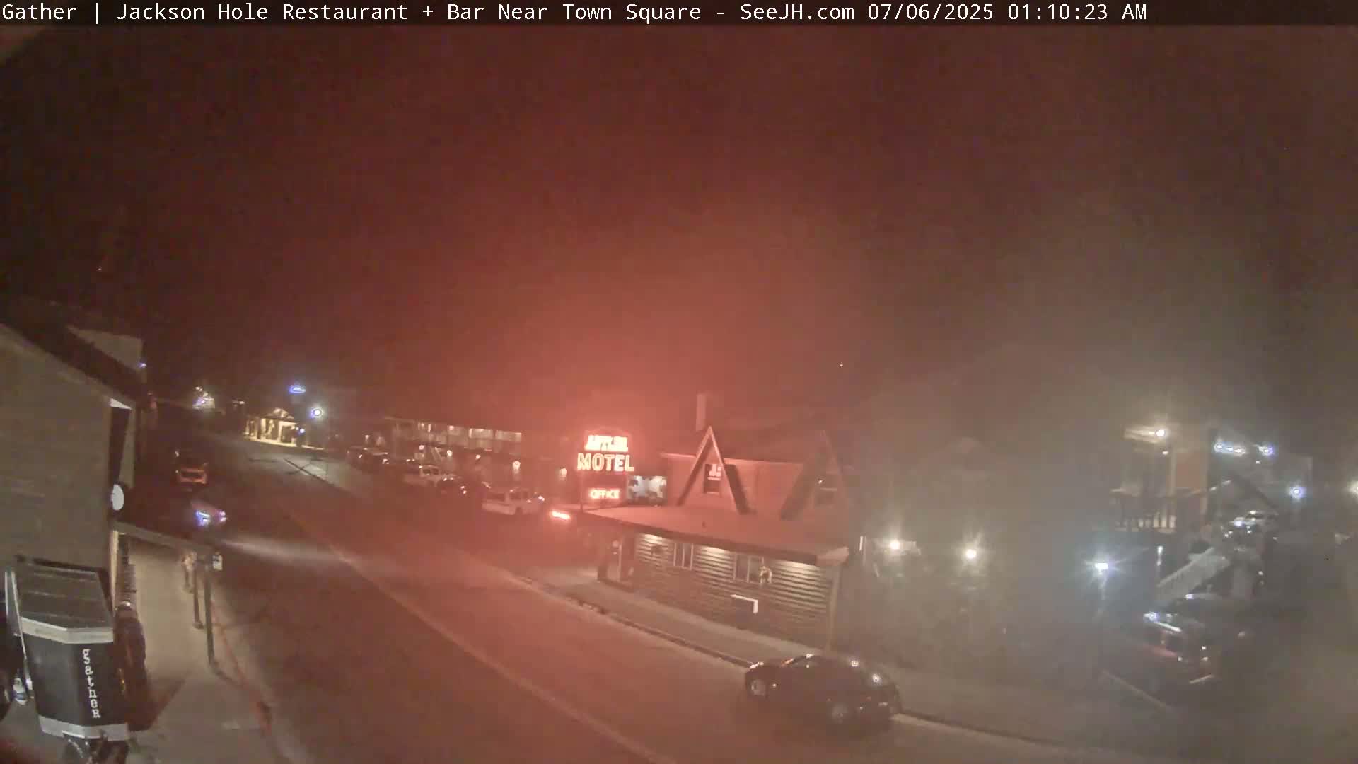 A foggy night scene shows a motel and other buildings along a road with a few cars visible.