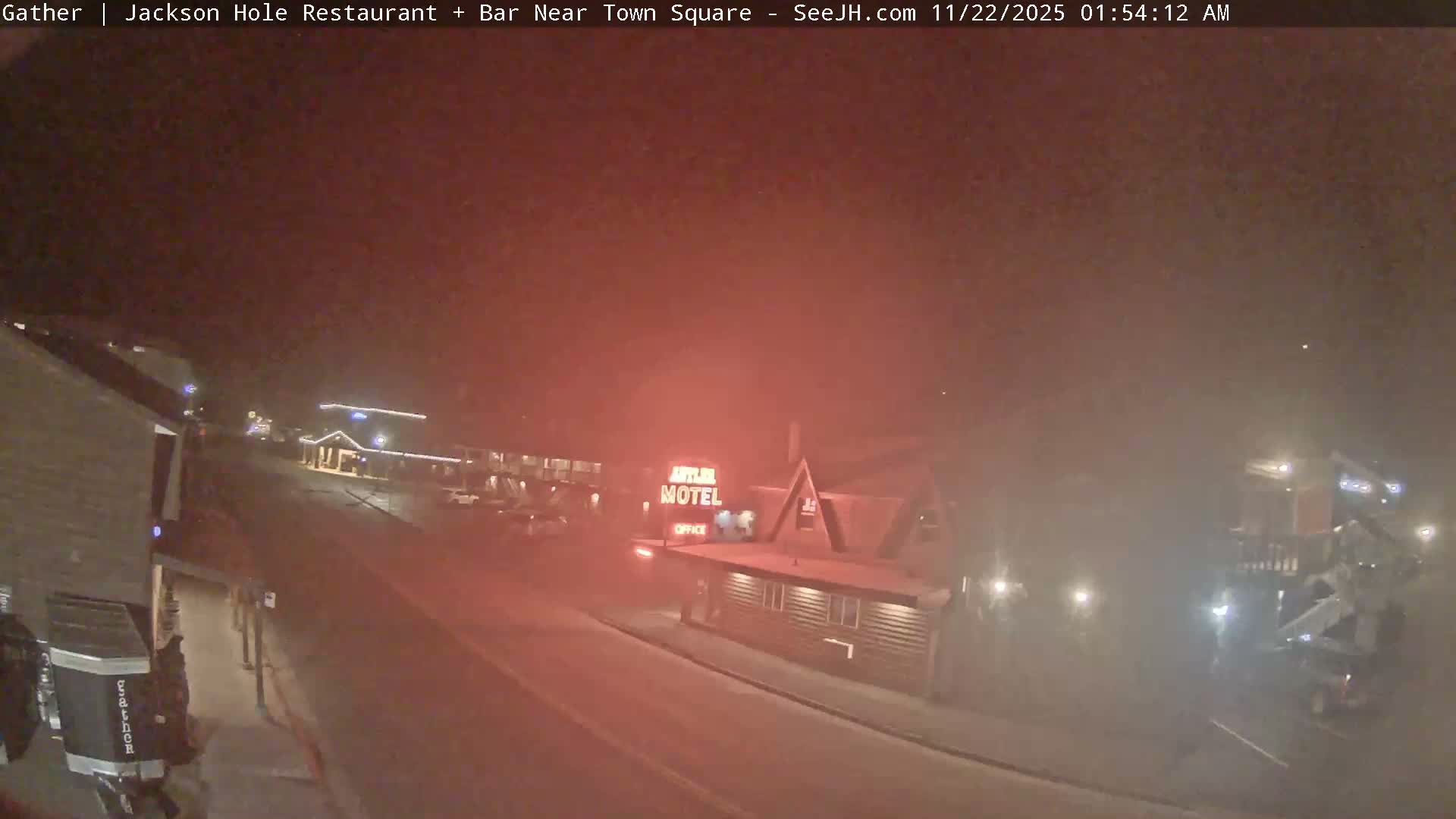 A foggy nighttime street scene features a red-glowing motel sign and several other illuminated buildings along a road, with heavy mist scattering the lights and obscuring distant views.