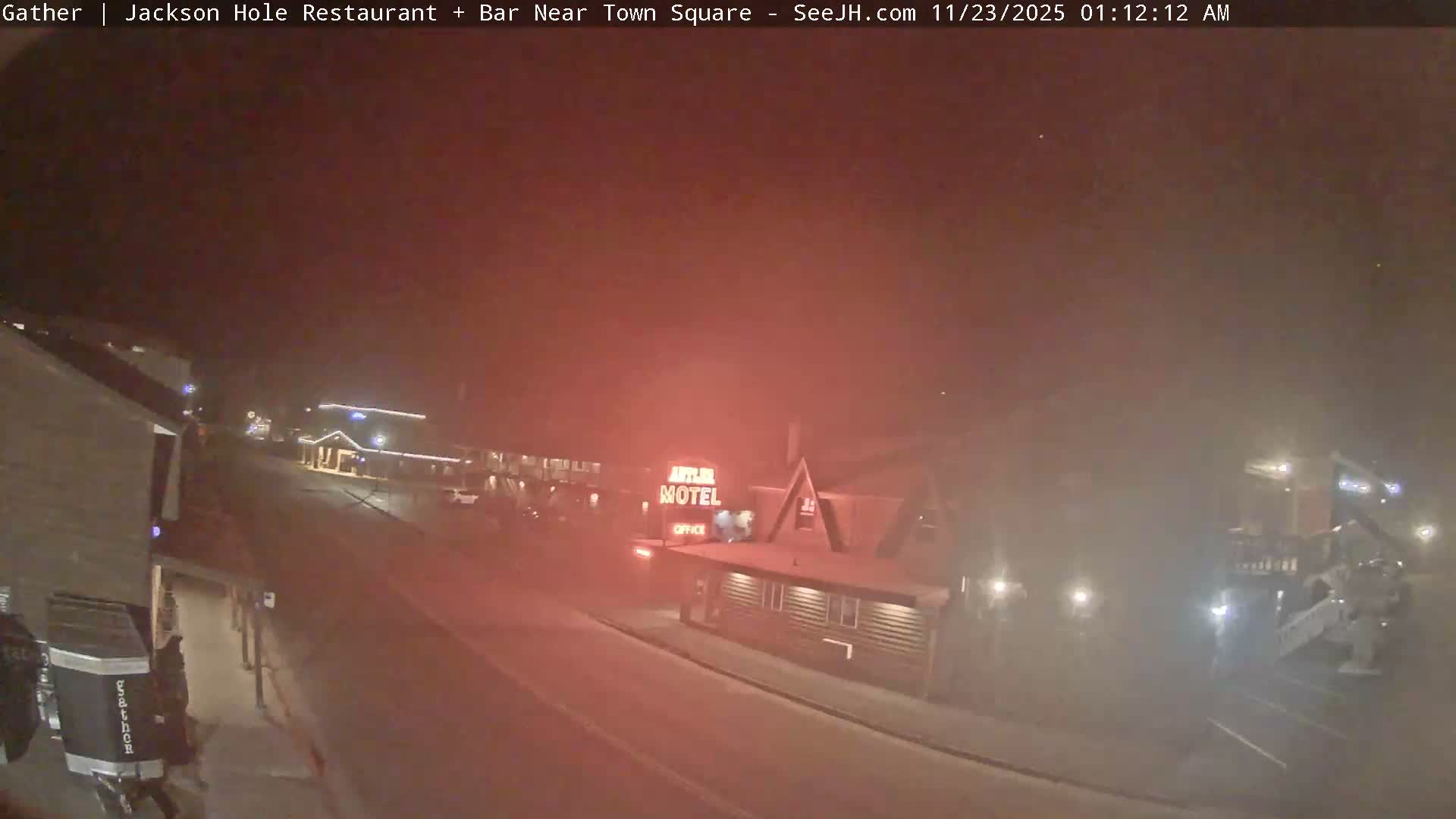 A street scene unfolds at night, shrouded in a reddish-brown haze or light fog, with the 'Antler Motel' sign and other buildings softly illuminated by artificial lights.