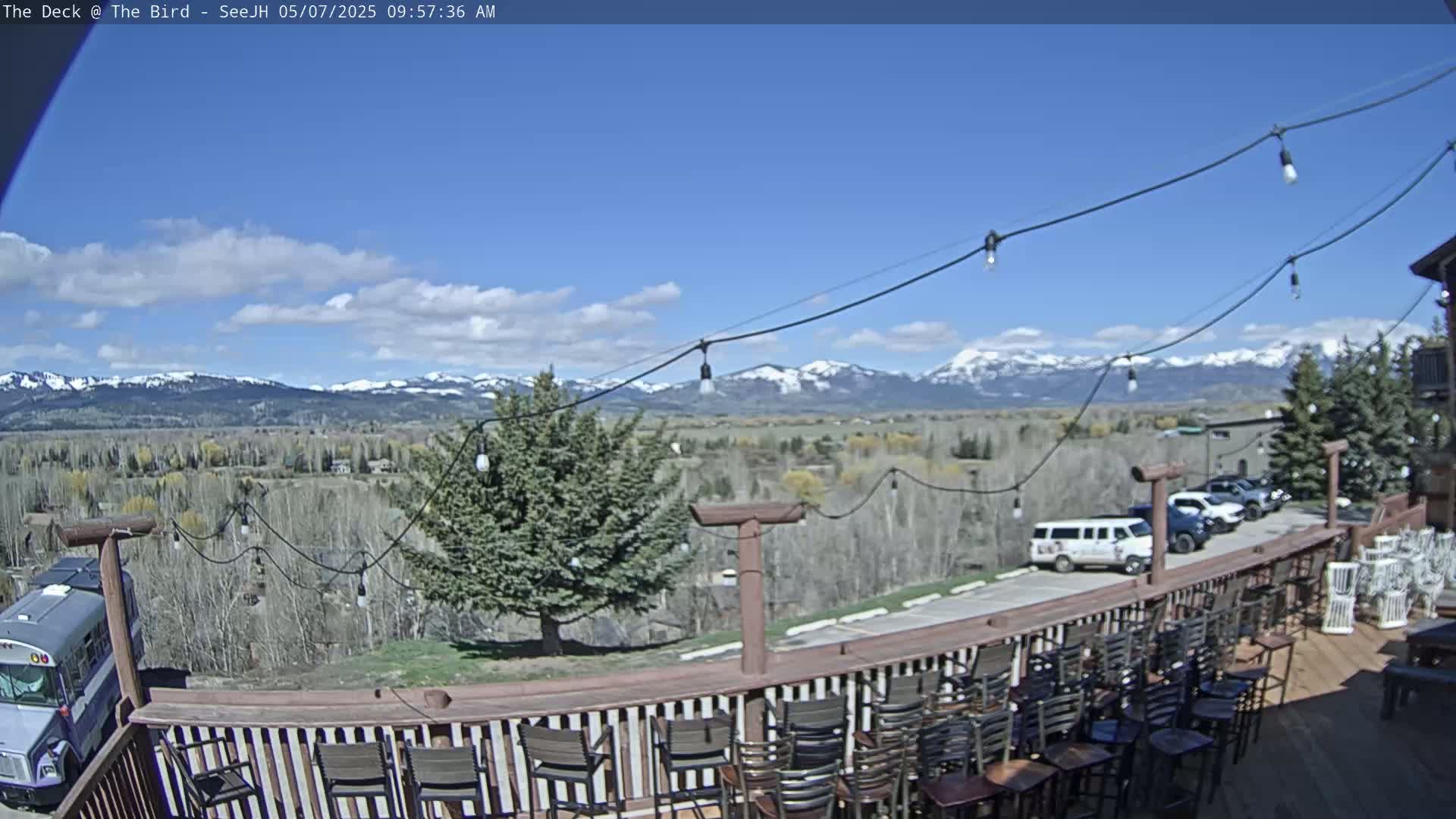 A deck with empty chairs overlooks a valley and snow-capped mountains under a mostly sunny sky.