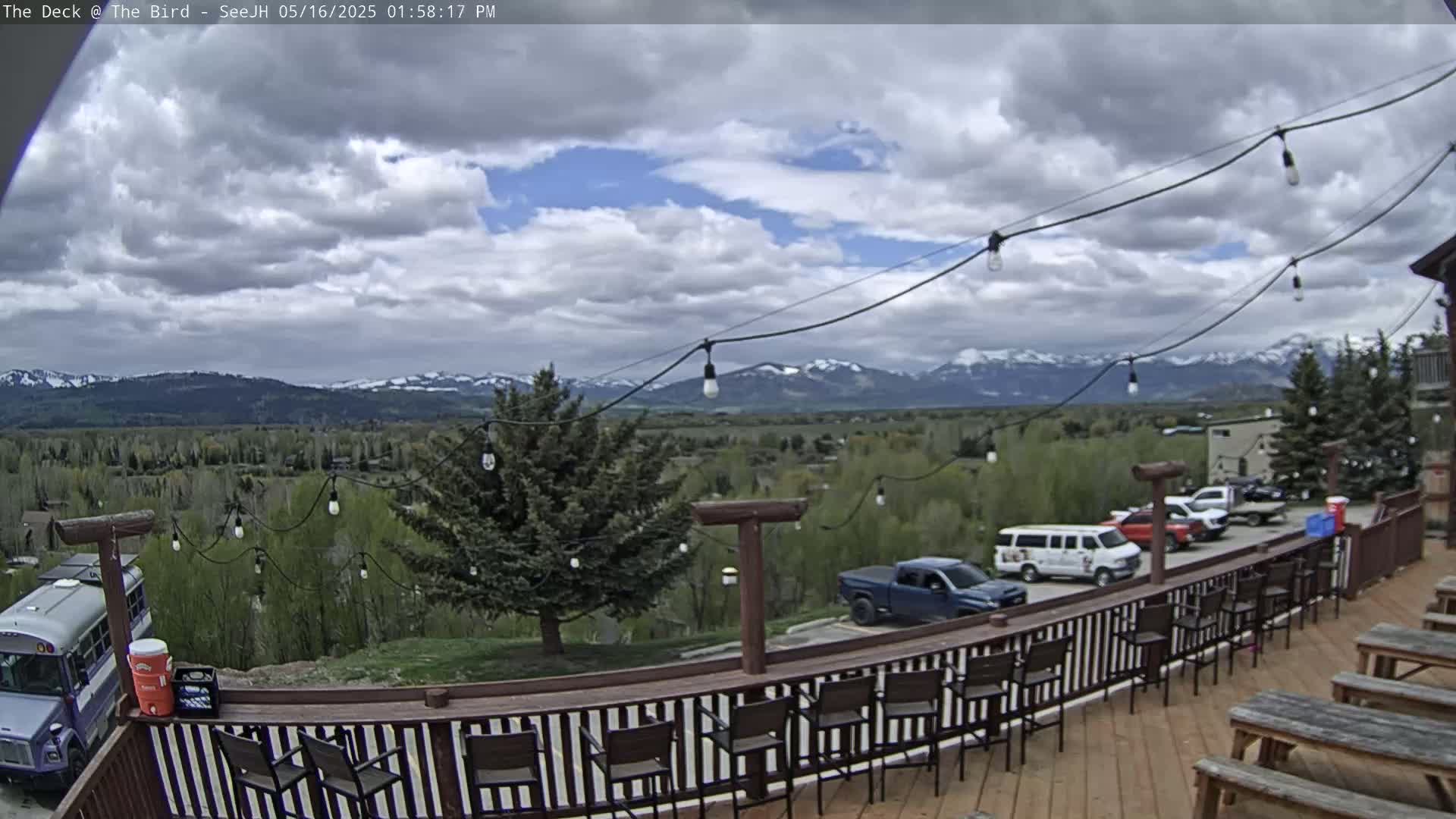 A deck with a bar and seating overlooks a valley with mountains in the distance under a partly cloudy sky.