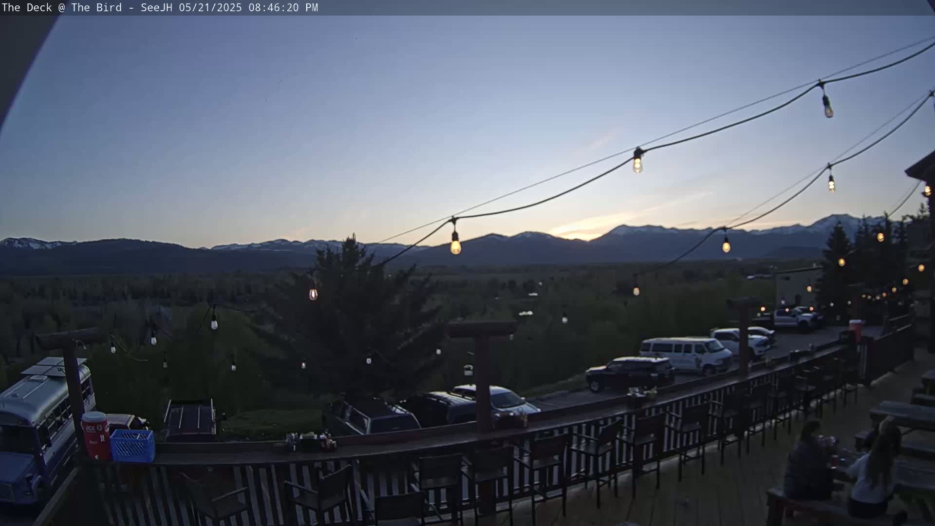An outdoor patio with string lights overlooks a valley and mountain range at dusk.