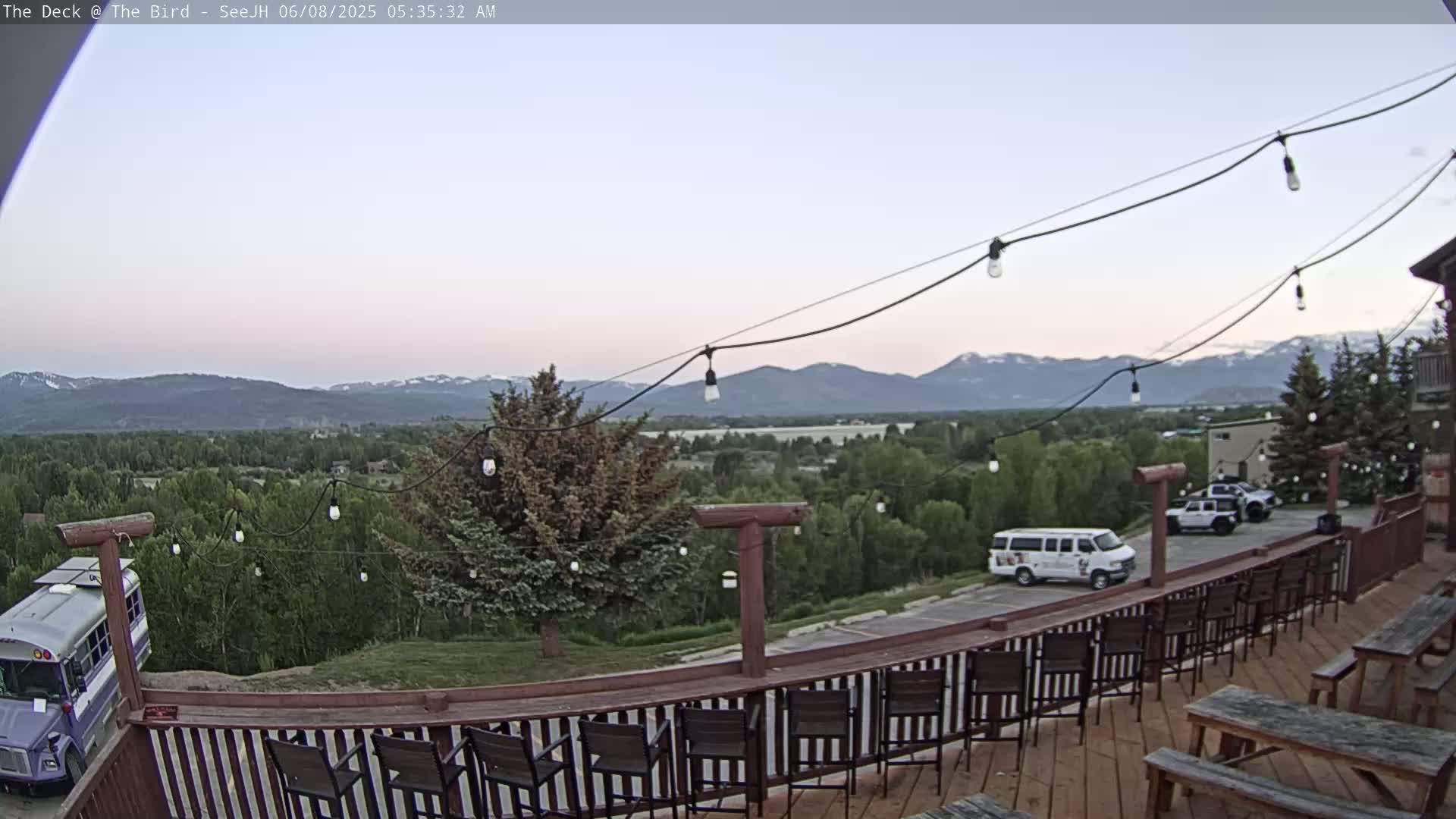 A wooden deck with string lights overlooks a valley and distant mountains under a clear, twilight sky.