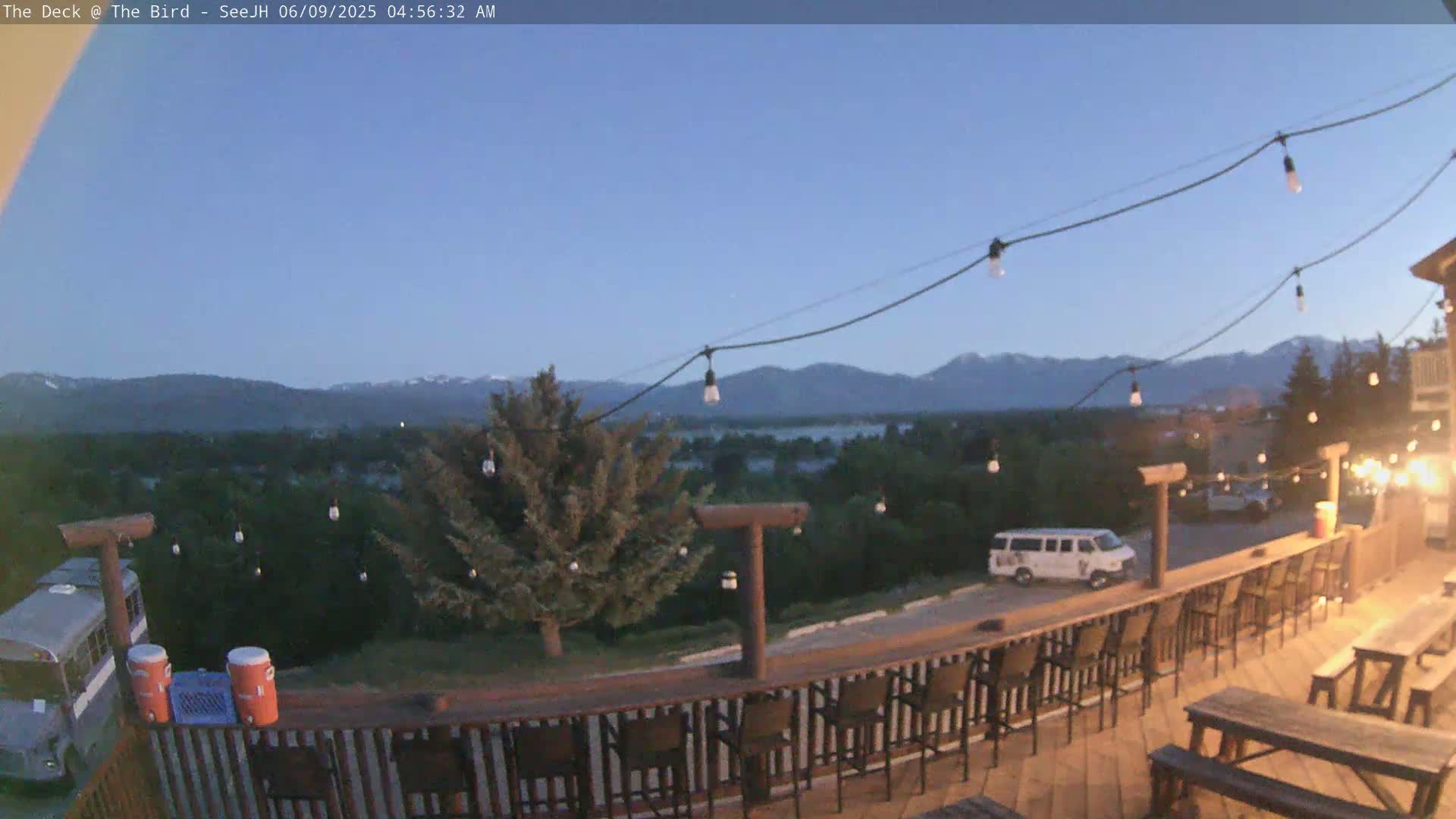An outdoor deck with string lights overlooks a valley and distant mountains under a twilight sky.
