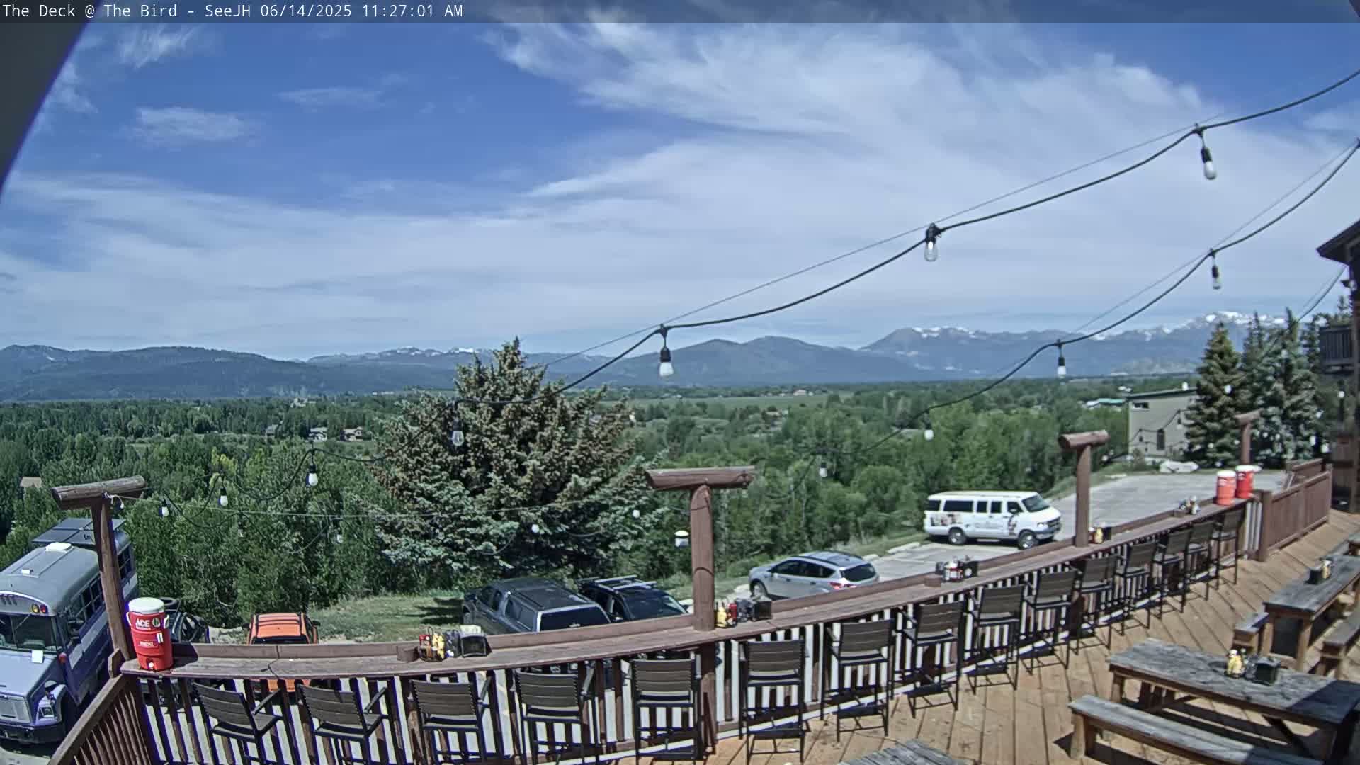 An outdoor deck with a bar and seating overlooks a valley and distant mountains under a partly cloudy sky.