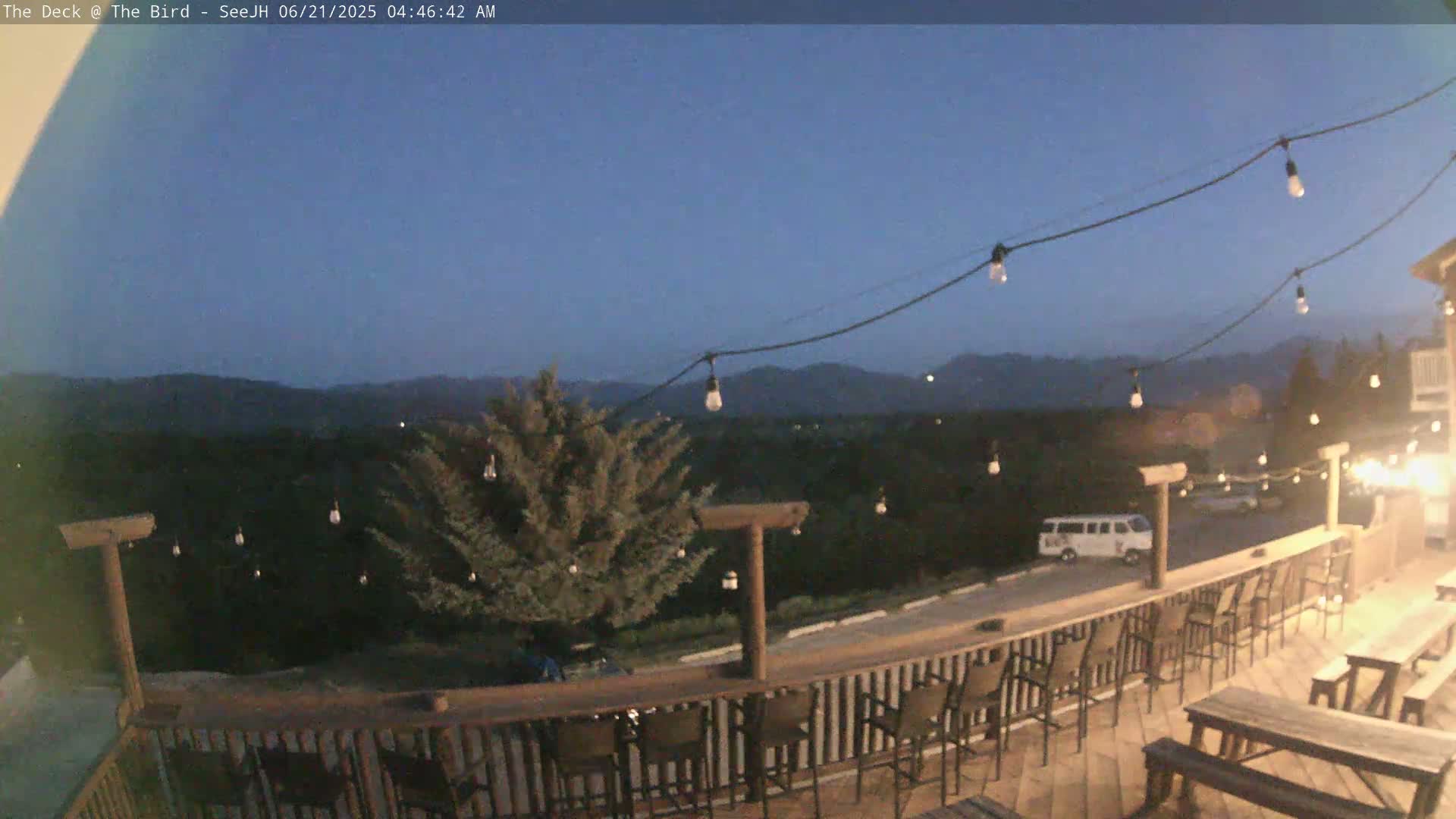 An outdoor deck with string lights overlooks a mountain range under a twilight sky.