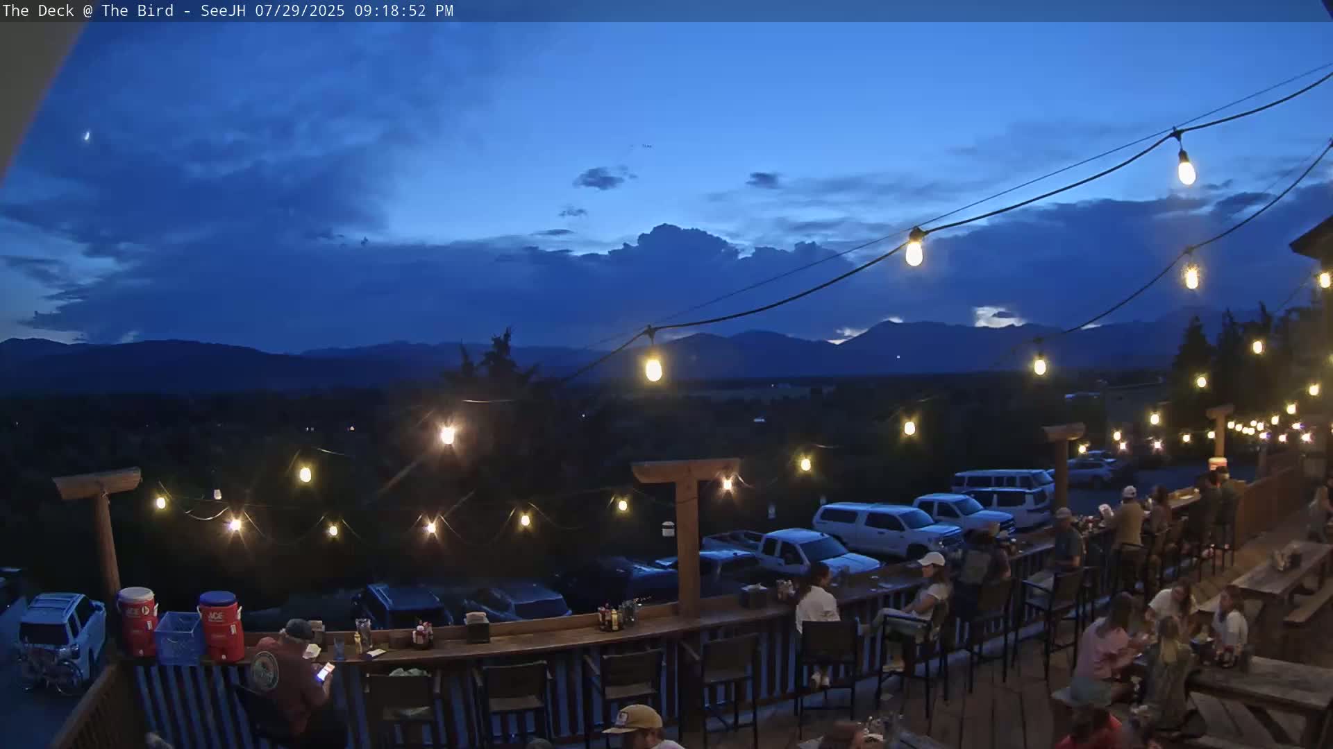 A nighttime outdoor scene shows a deck with empty bar stools and picnic tables under a dark, clear sky.