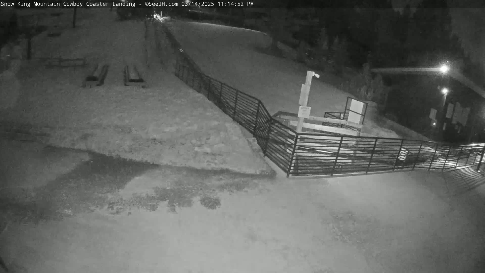 A snow-covered area at night, with a metal railing and a dark building in the background.