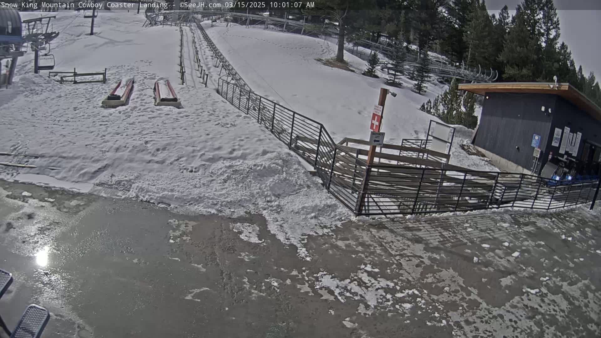 A snowy mountain scene shows a coaster landing area with two empty sleds, a nearby building, and a partially icy ground.