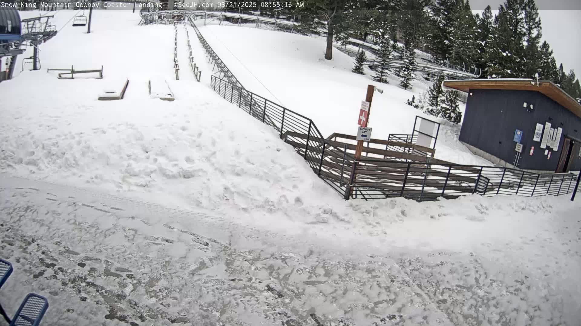 A snow-covered area with a coaster track, fences, and a small building under an overcast sky.