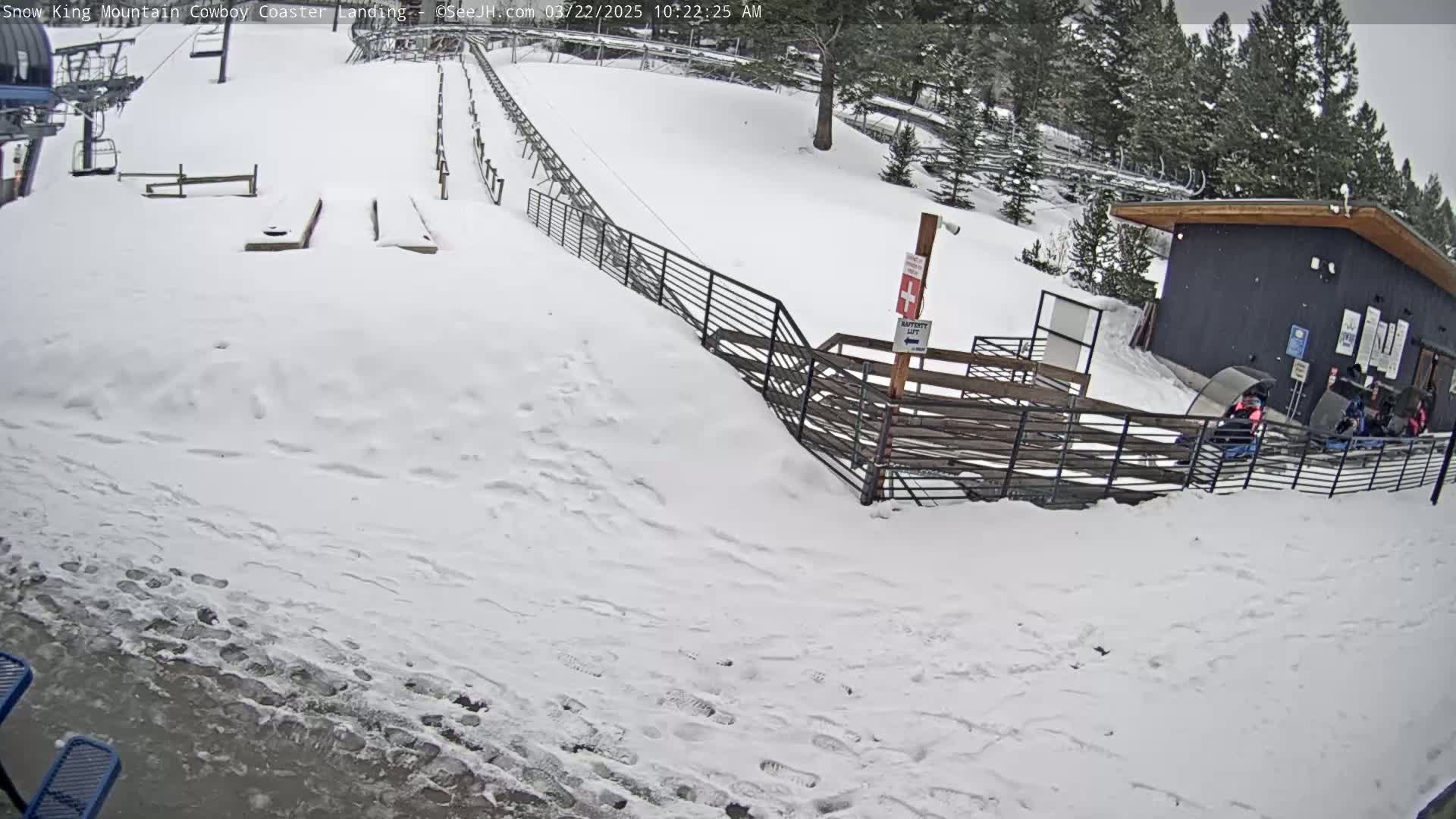 A snow-covered area with a coaster lift, a small building, and several people near the base of a hill.