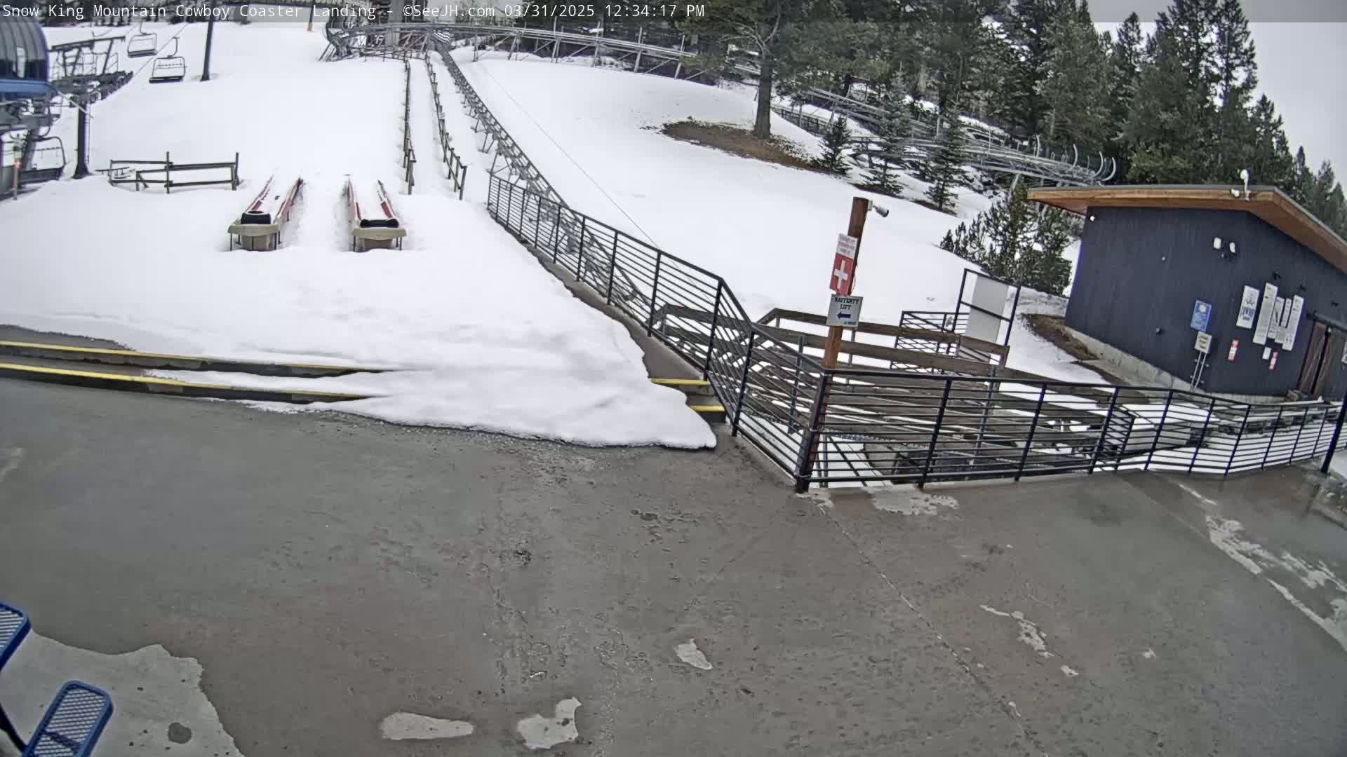 A snow-covered area with a paved landing, two empty coaster carts, and a dark building in the background.