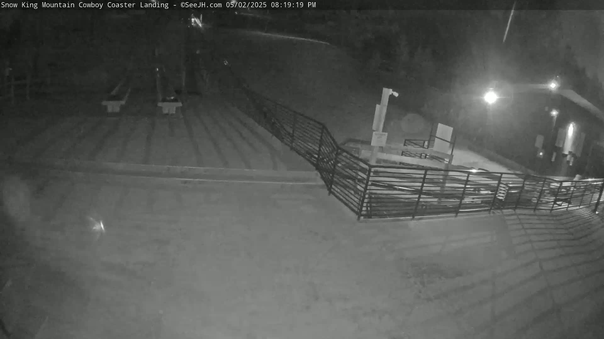A nighttime, low-light view shows an empty area with benches, stairs, and a railing, illuminated by artificial light.
