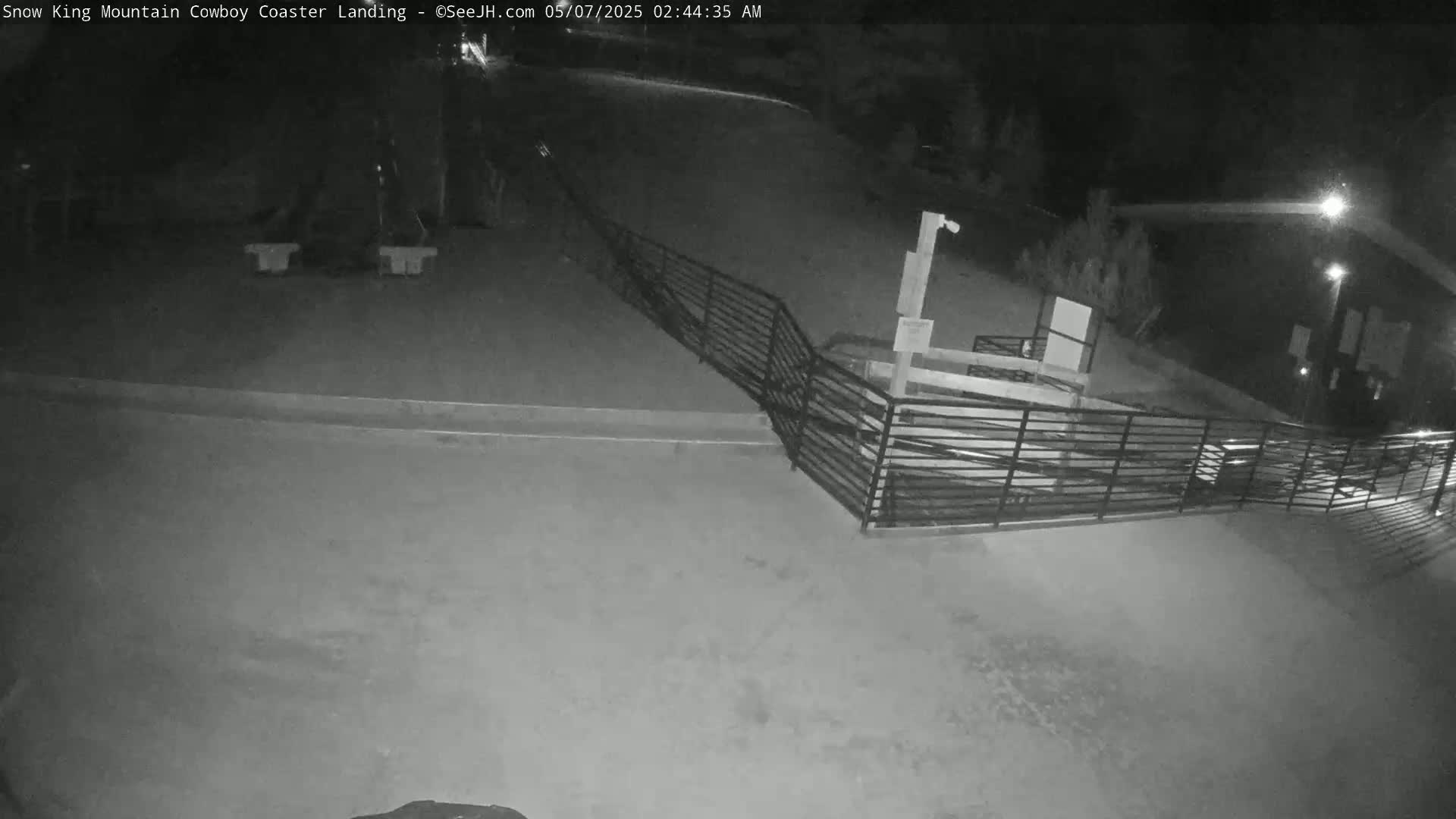 A nighttime, low-light view of an empty paved area with a metal railing and a building in the background.