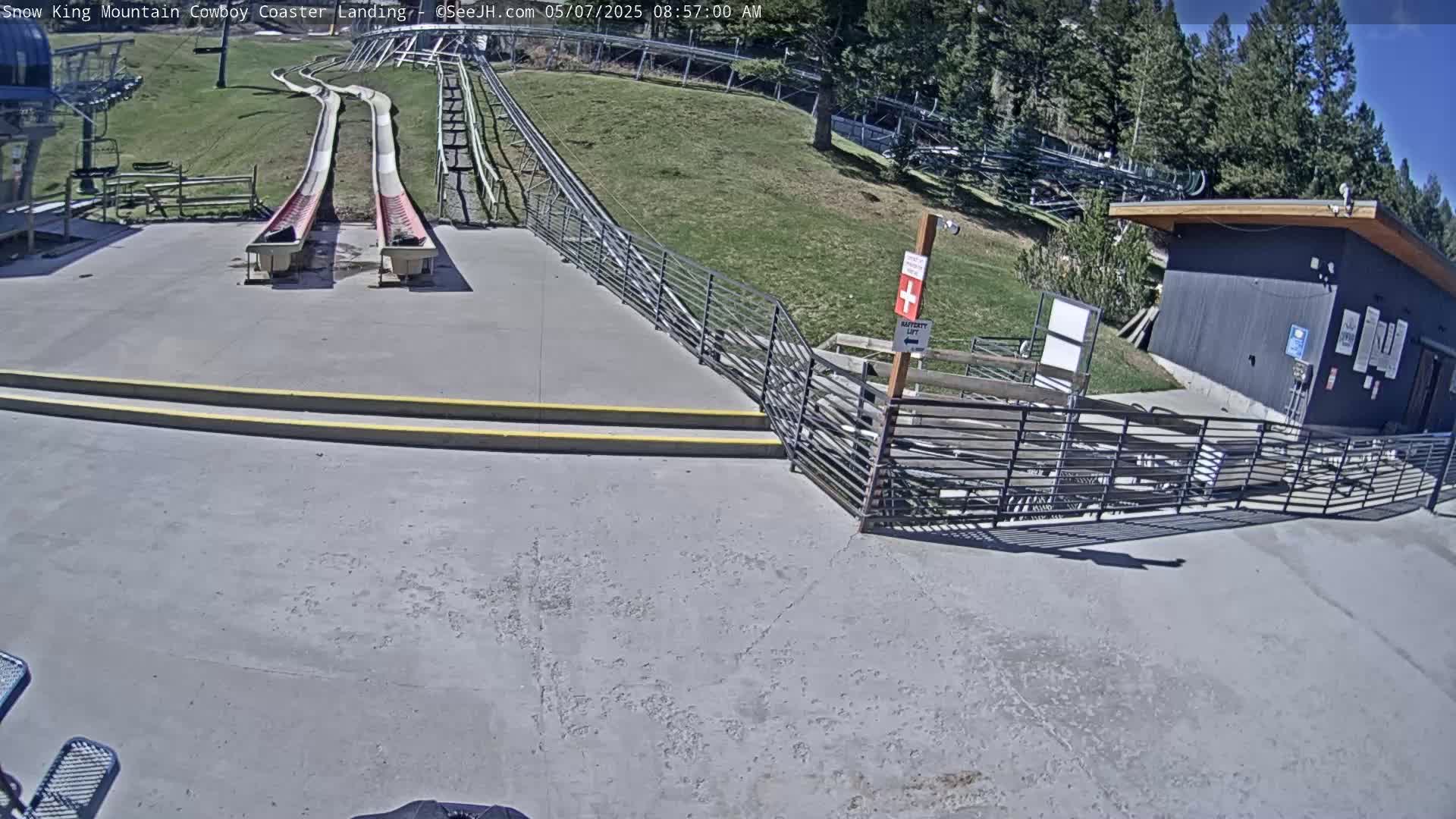 Two empty, red-and-white slides end at a paved area next to a small building, all under a sunny sky.
