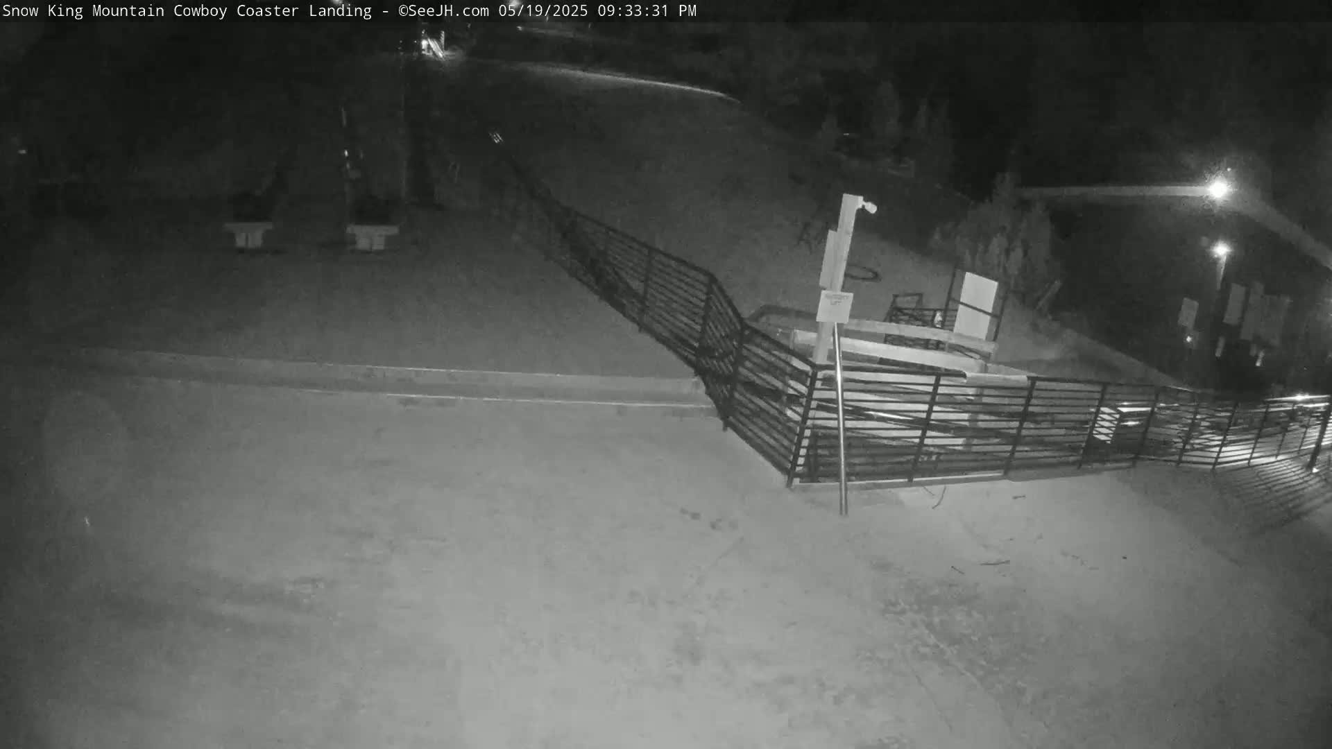 A nighttime, low-angle view shows a dark, empty area with a metal railing and a building in the background.