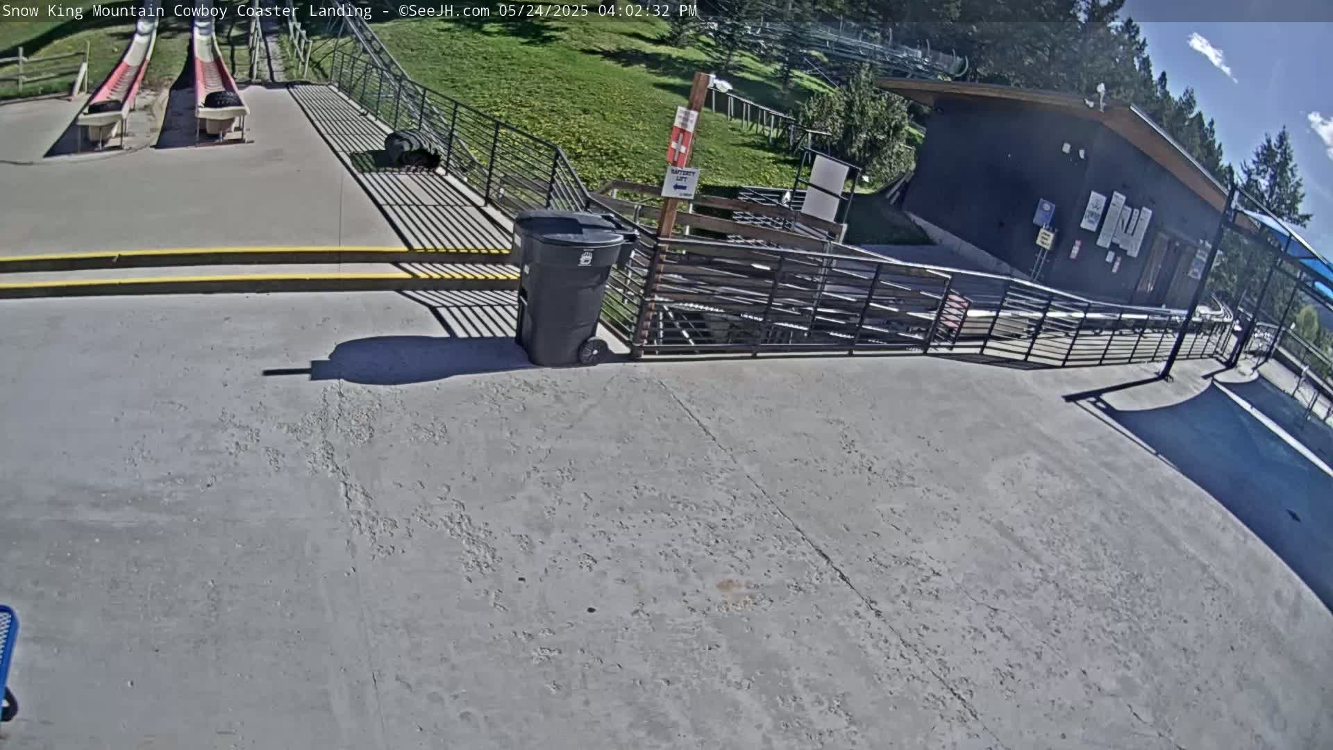 A paved area with two coaster tracks, a small building, and a trash can, all under a sunny sky.