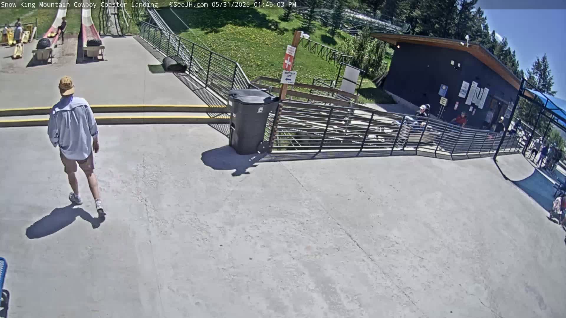 A person walks away from a light gray paved area near a coaster landing, under a sunny sky.