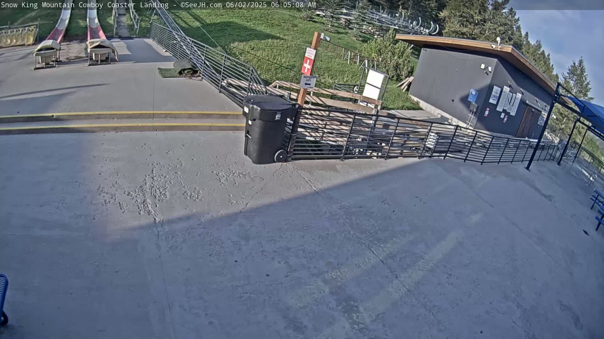 A paved landing area with two red slides, a small building, and a metal fence is visible under a mostly sunny sky.