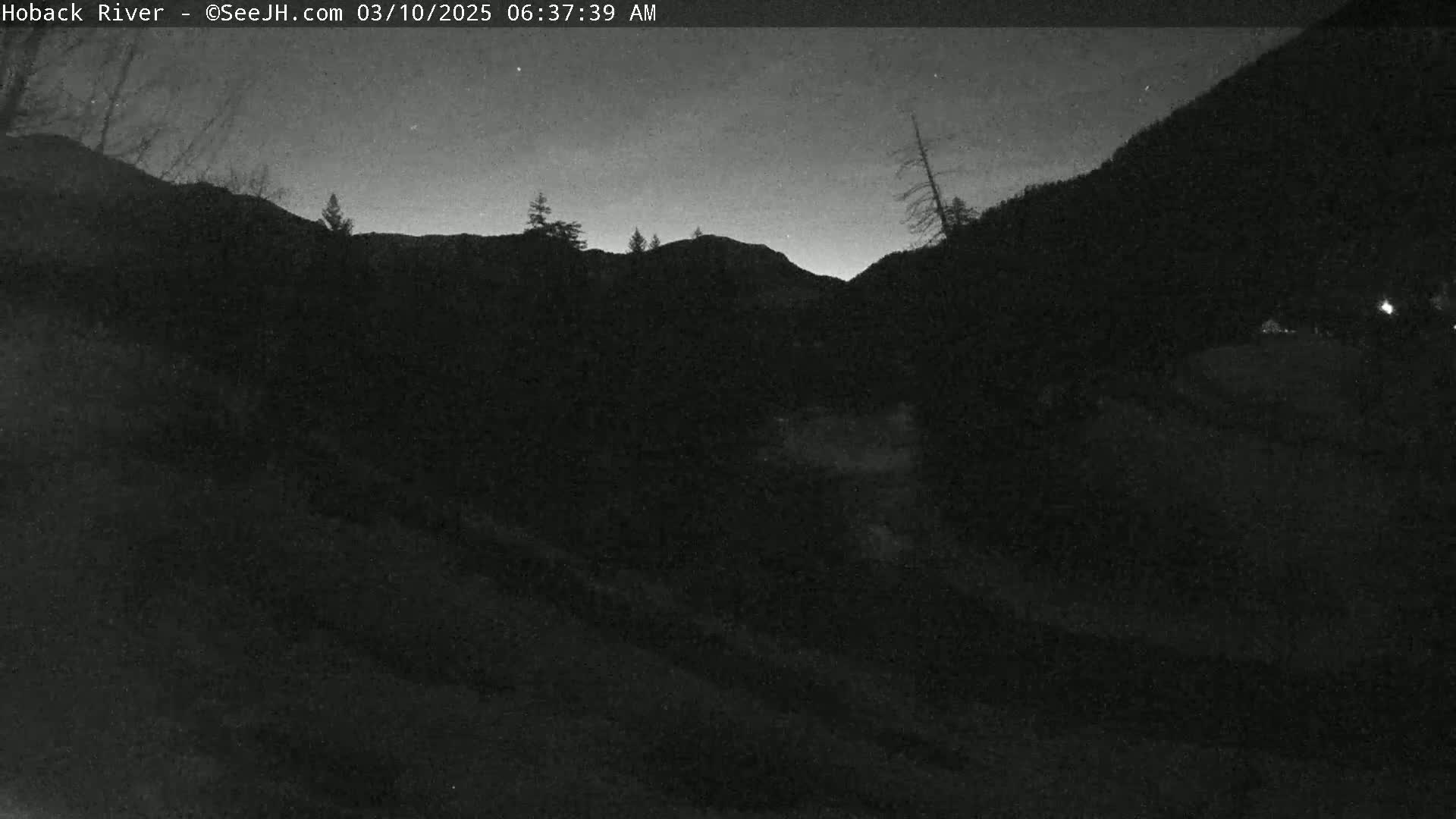 A dark, nighttime view of a mountainous landscape under a clear, starlit sky.