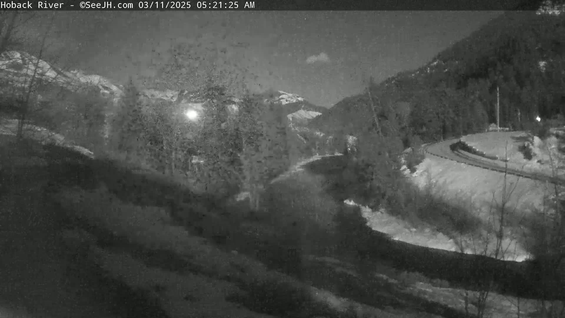A nighttime, low-light view of a river curving through a snow-dusted mountain valley.