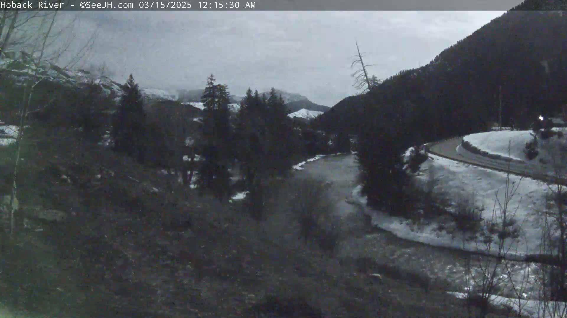A river flows through a snowy mountain valley under an overcast sky.