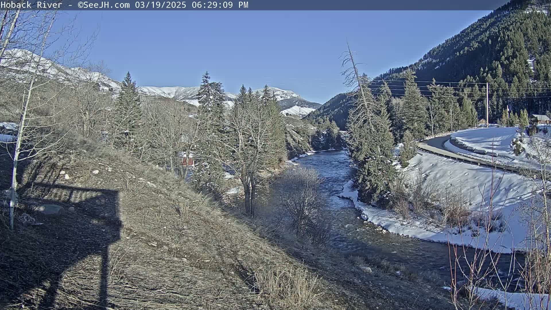 A river flows through a snowy mountain valley under a clear blue sky.