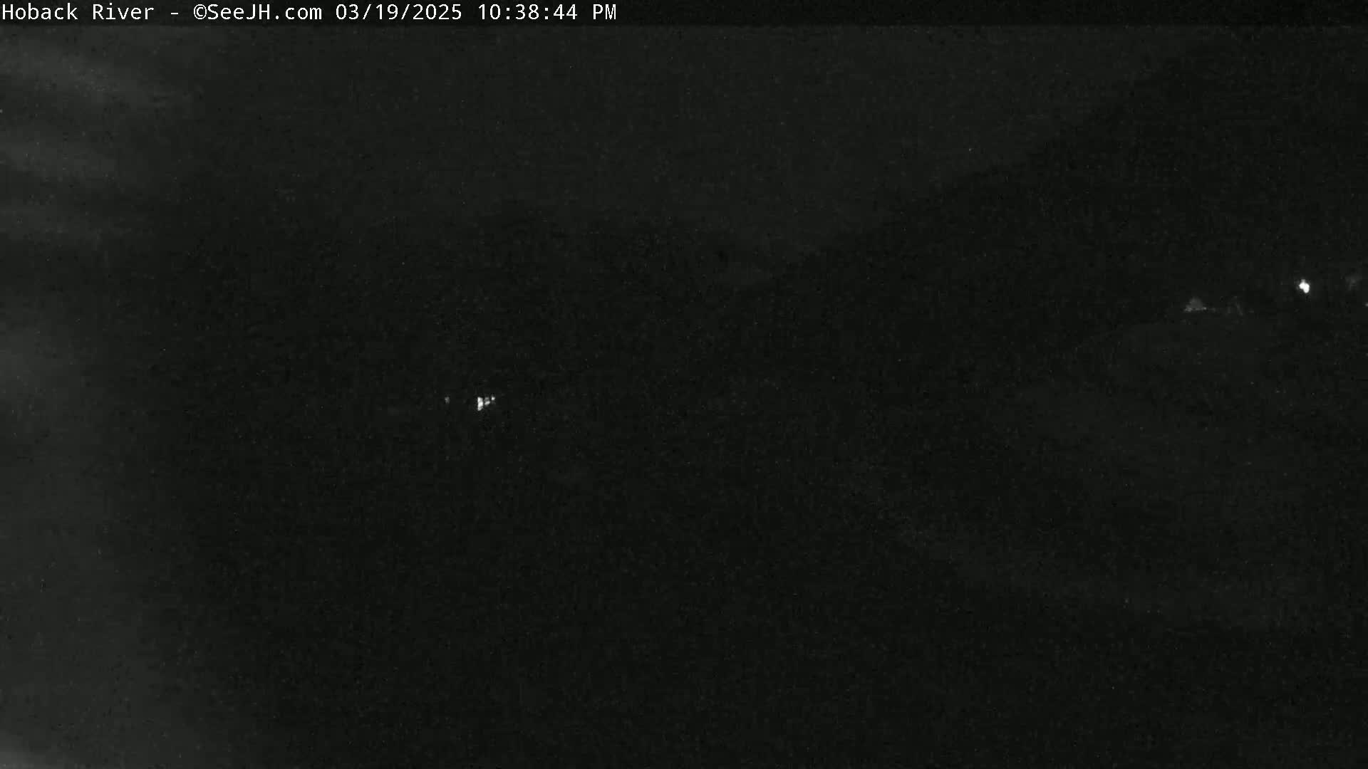 A nighttime, low-light view shows a dark landscape with a few distant, faint lights.