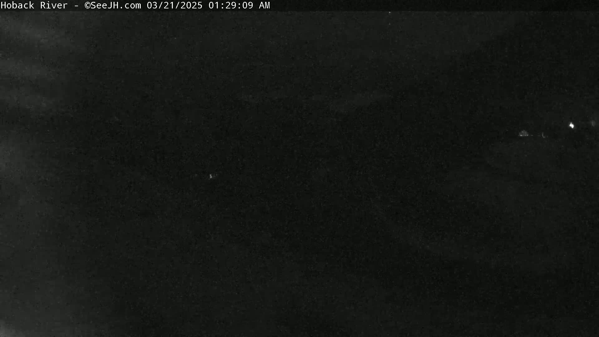 A nighttime long shot of a dark, possibly overcast, landscape with a few faint lights visible in the distance.