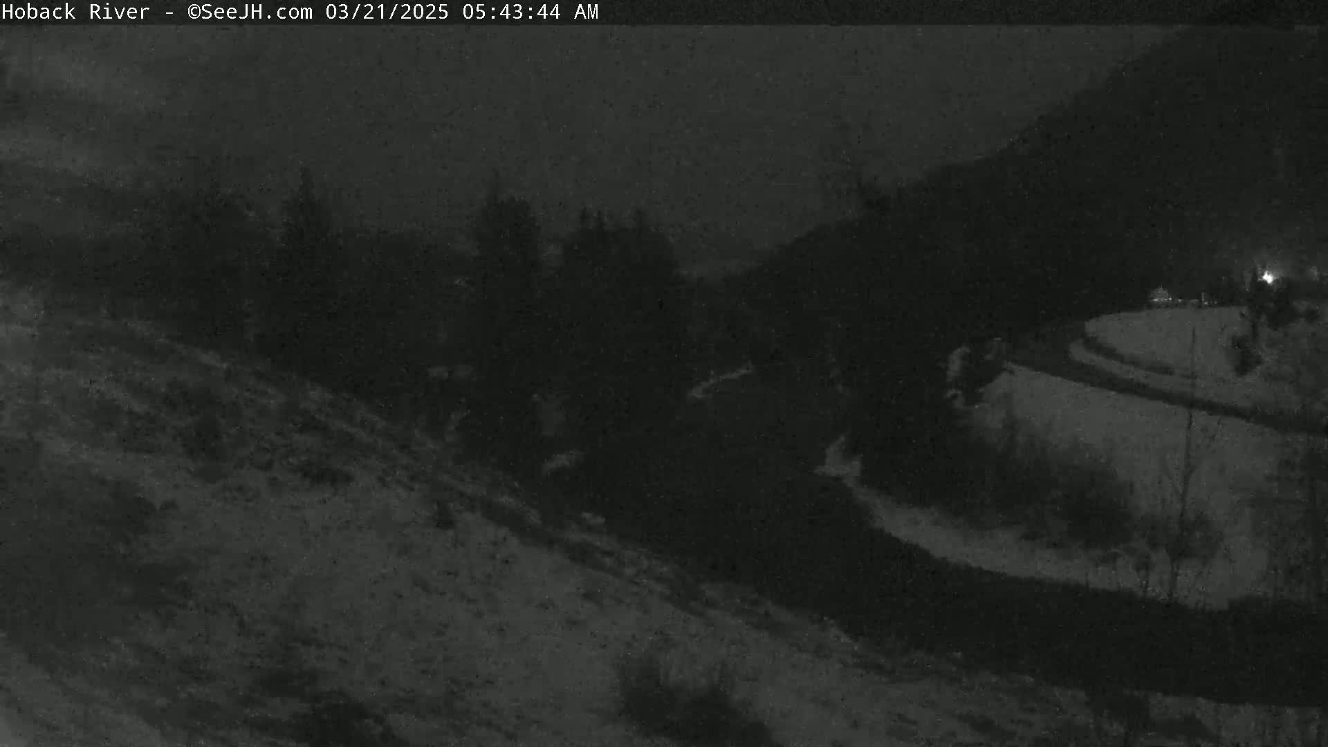 A nighttime, snow-covered landscape is shown, with a dark road curving through it.