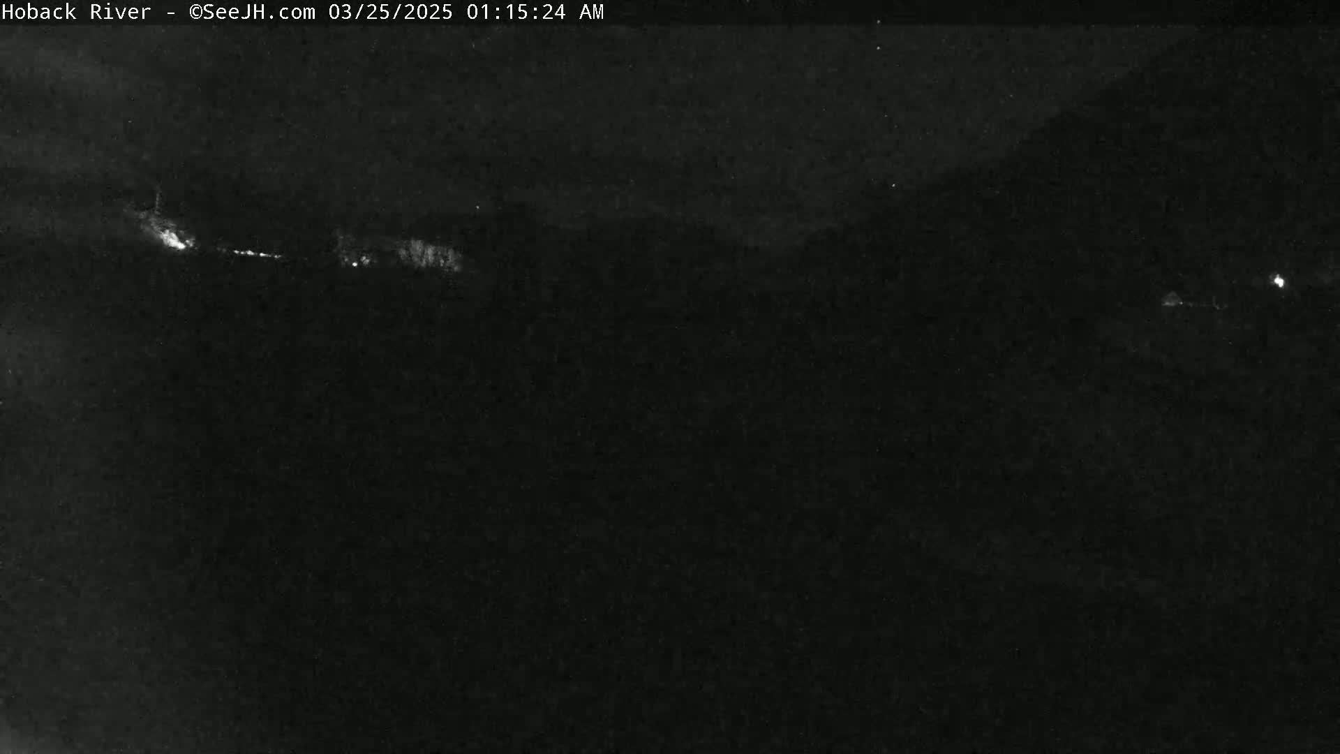 A nighttime, low-light image shows a dark landscape with a few faint lights in the distance.