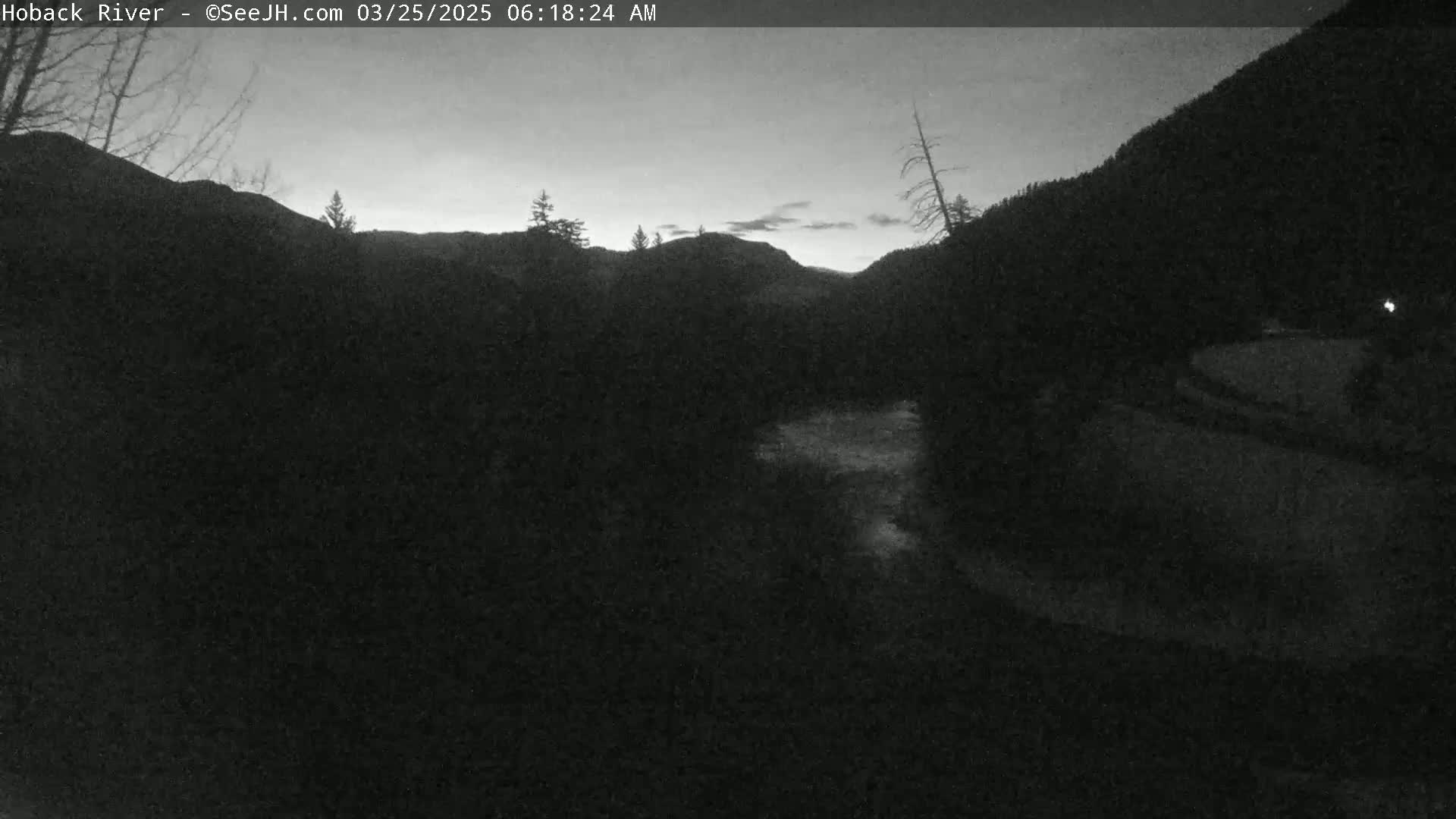 A dark, pre-dawn view of a river flowing through a valley between mountains, under a dusky sky.