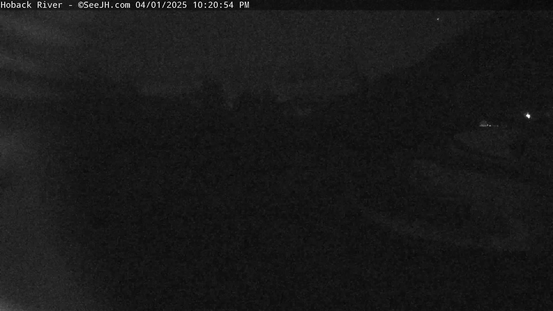 A dark, nighttime outdoor scene shows a low-light view of an indistinct landscape under a mostly clear sky.
