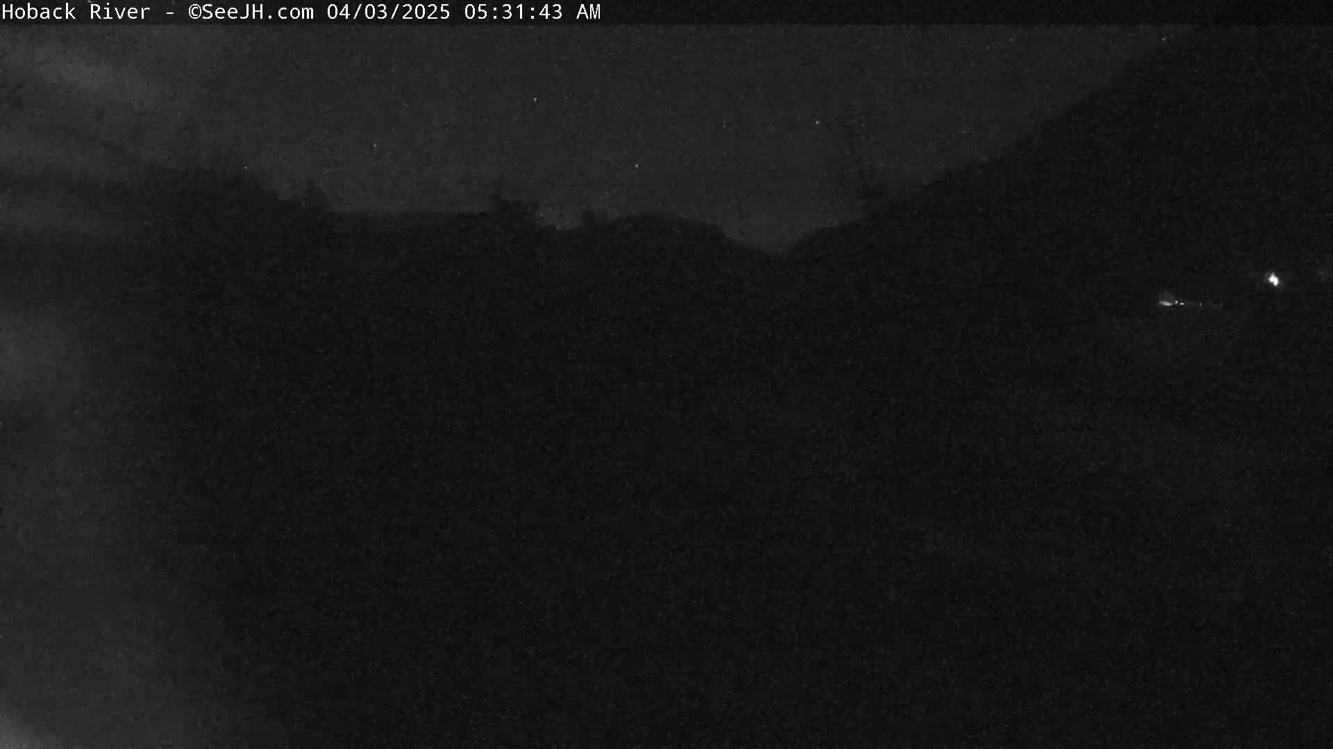 A dark, nighttime scene shows a distant, silhouetted landscape under a mostly clear sky.