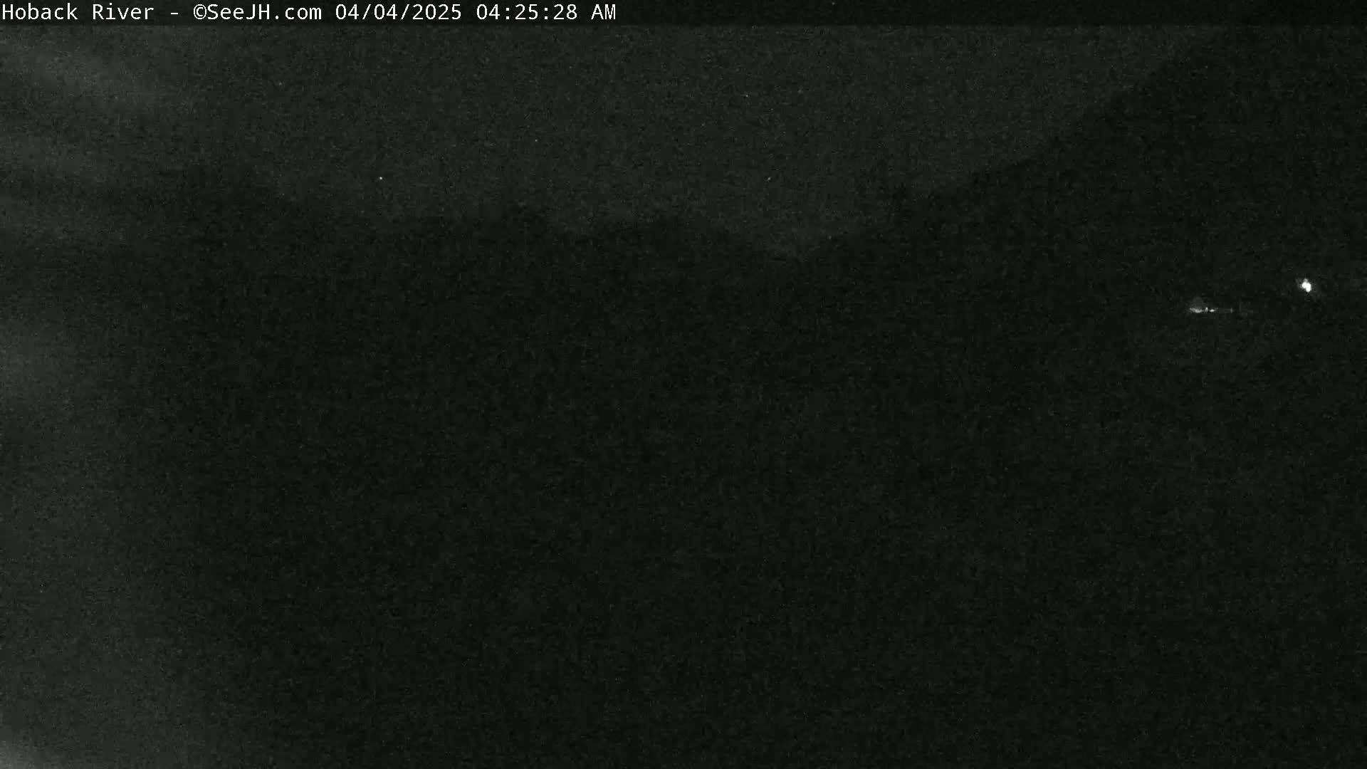 A nighttime, low-light image shows a dark, indistinct landscape.