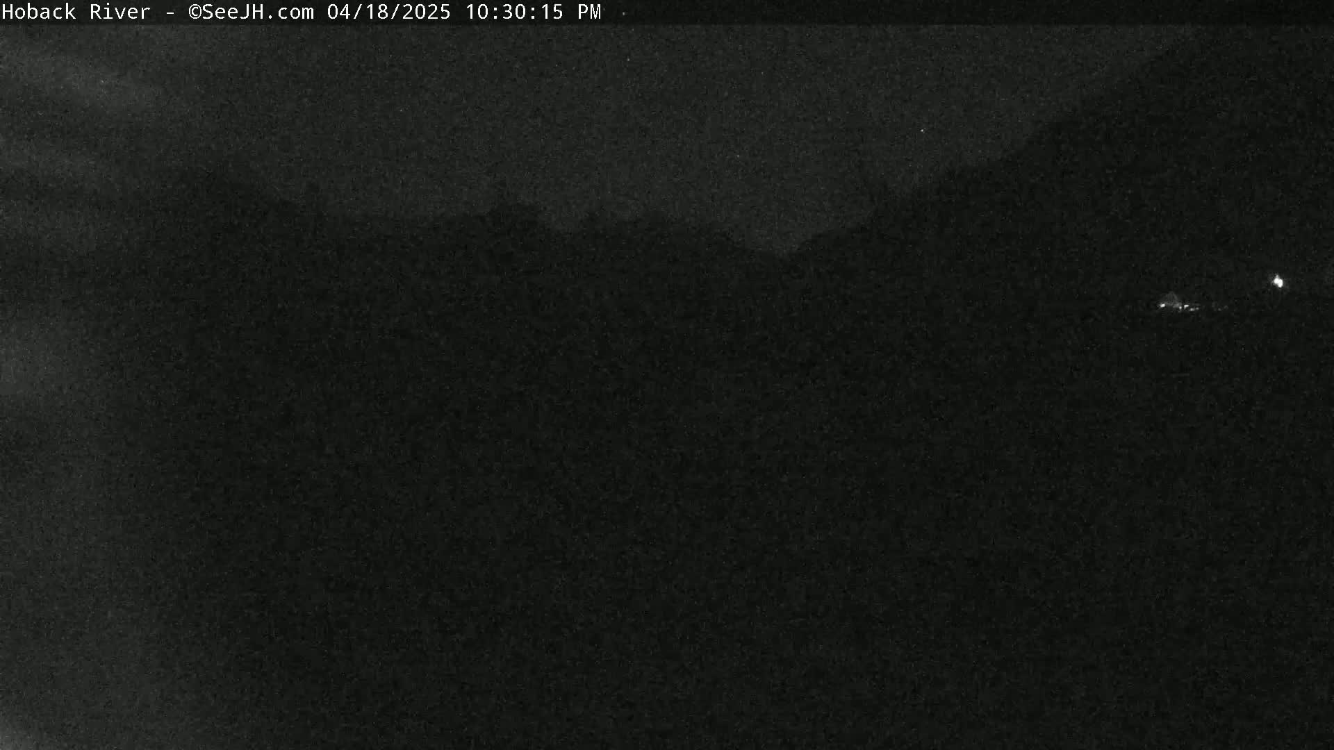 A nighttime, low-light image shows dark, indistinct hills or mountains under a cloudy sky.
