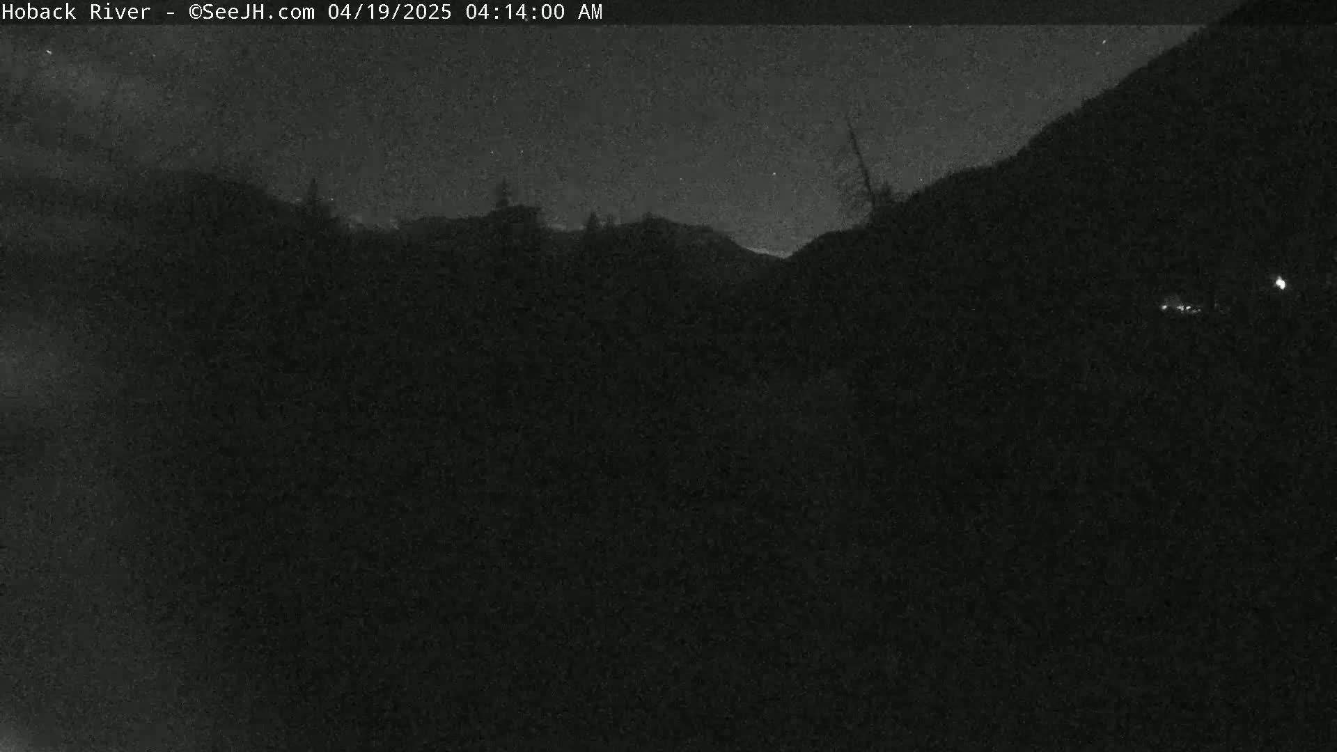 A dark, nighttime view of a landscape shows a silhouetted hillside under a mostly clear, starlit sky.